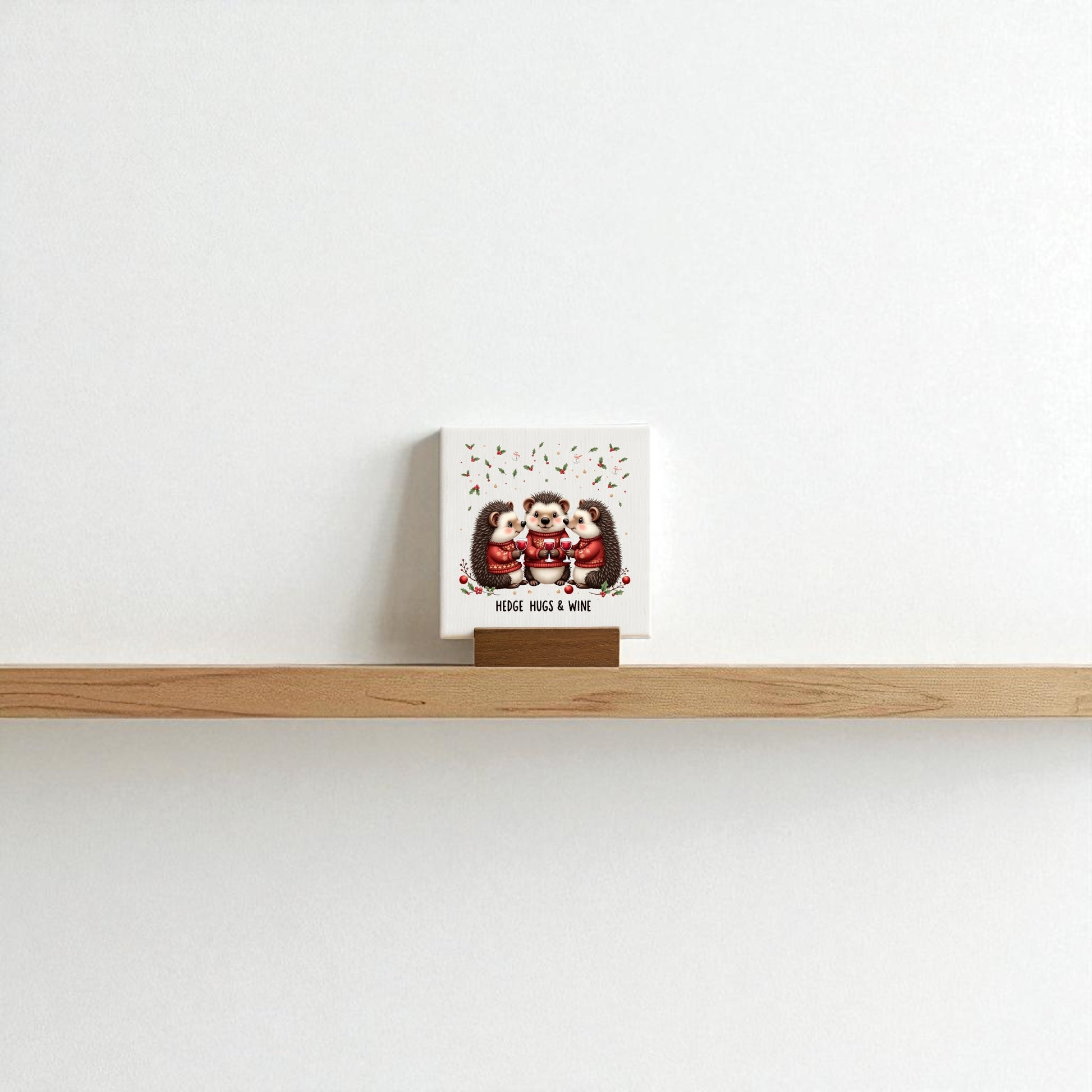 The Hedge Hugs & Wine Canvas Sign by Mirabilia Boutique is a 4x4 square card featuring three illustrated owls and "Merry, Wise & Wine"—a perfect festive holiday gift for wine lovers, displayed on a minimalist shelf against a white wall.