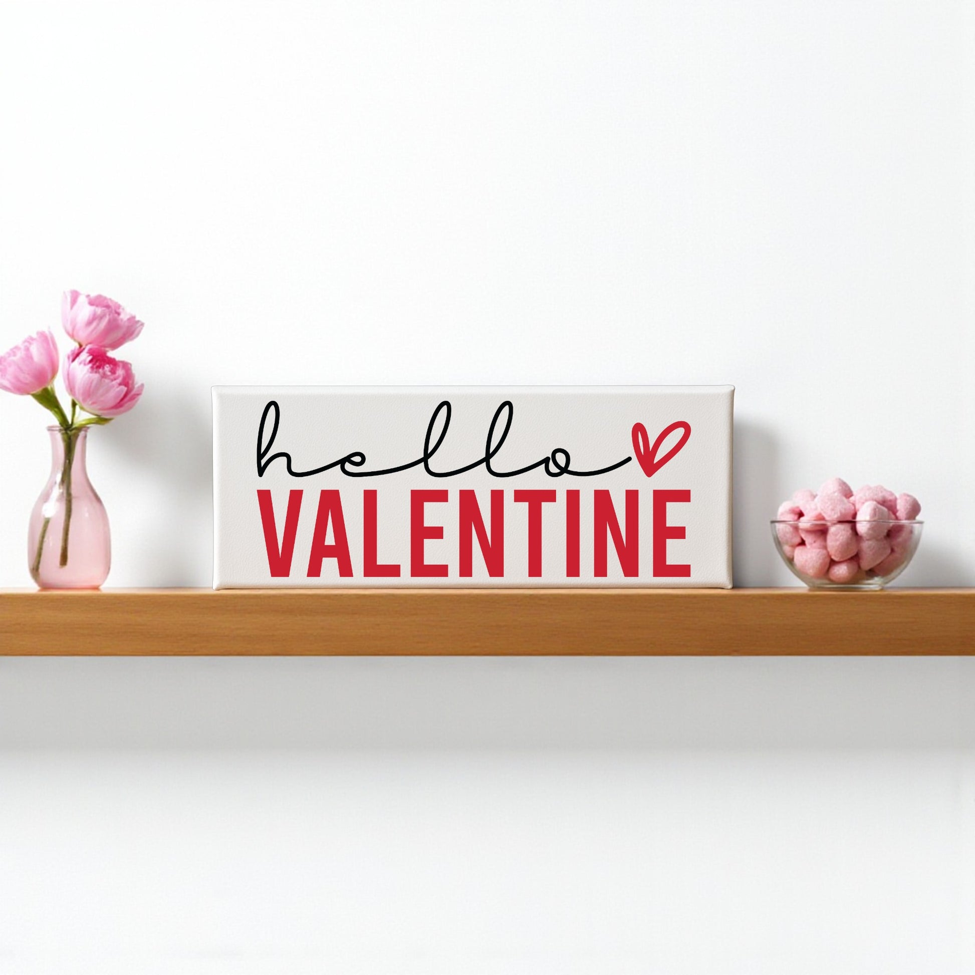 Mirabilia Boutique’s Hello Valentine Sign—modern red & white shelf decor—paired with pink flowers and a candy bowl, brings romantic Valentine’s Day charm to your wooden shelf.
