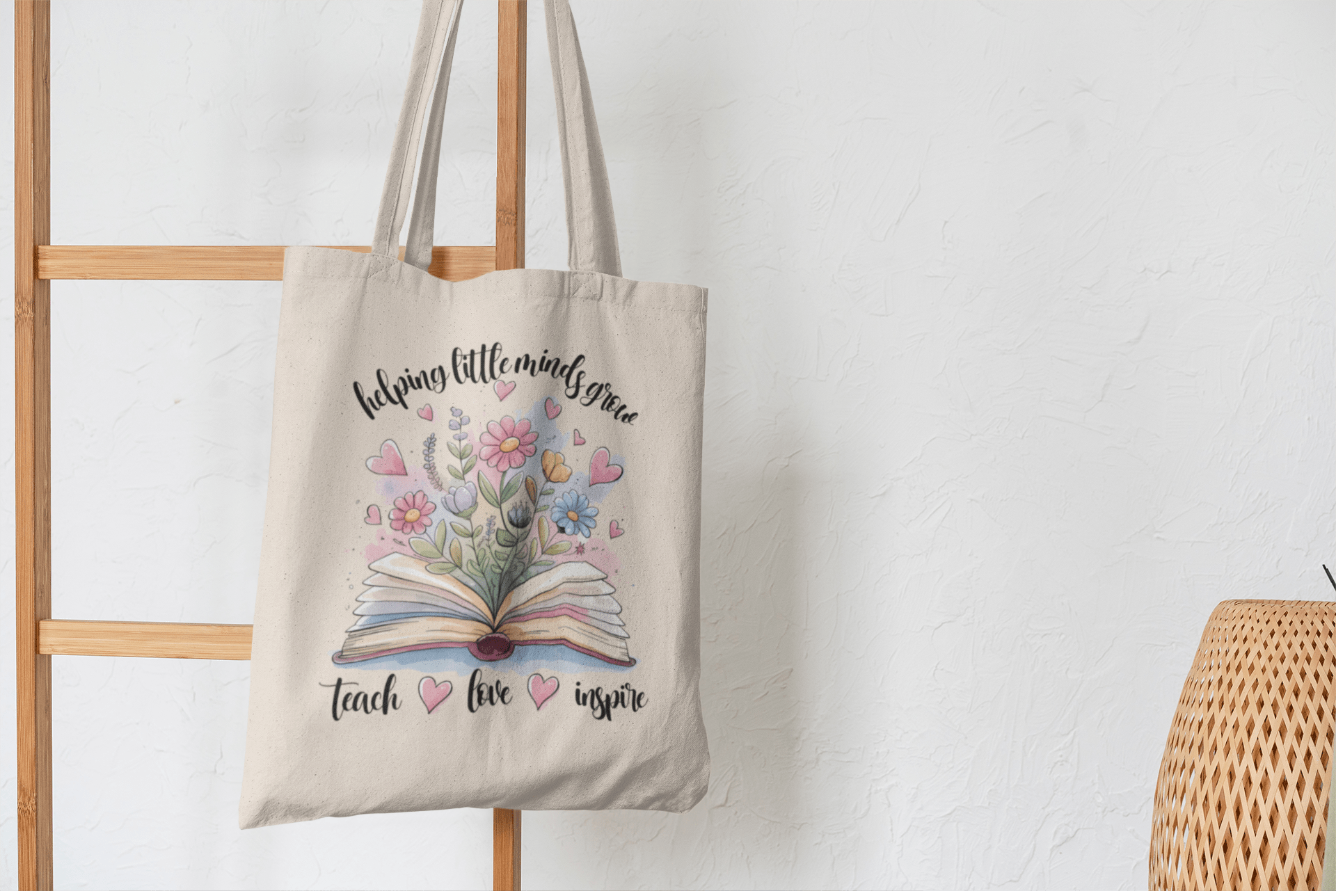 The Helping Little Minds Grow Tote Bag by Mirabilia Boutique is a beige canvas teacher bag with a book and floral design, plus the phrase "helping little minds grow, teach, love, inspire"—a perfect teacher appreciation gift.
