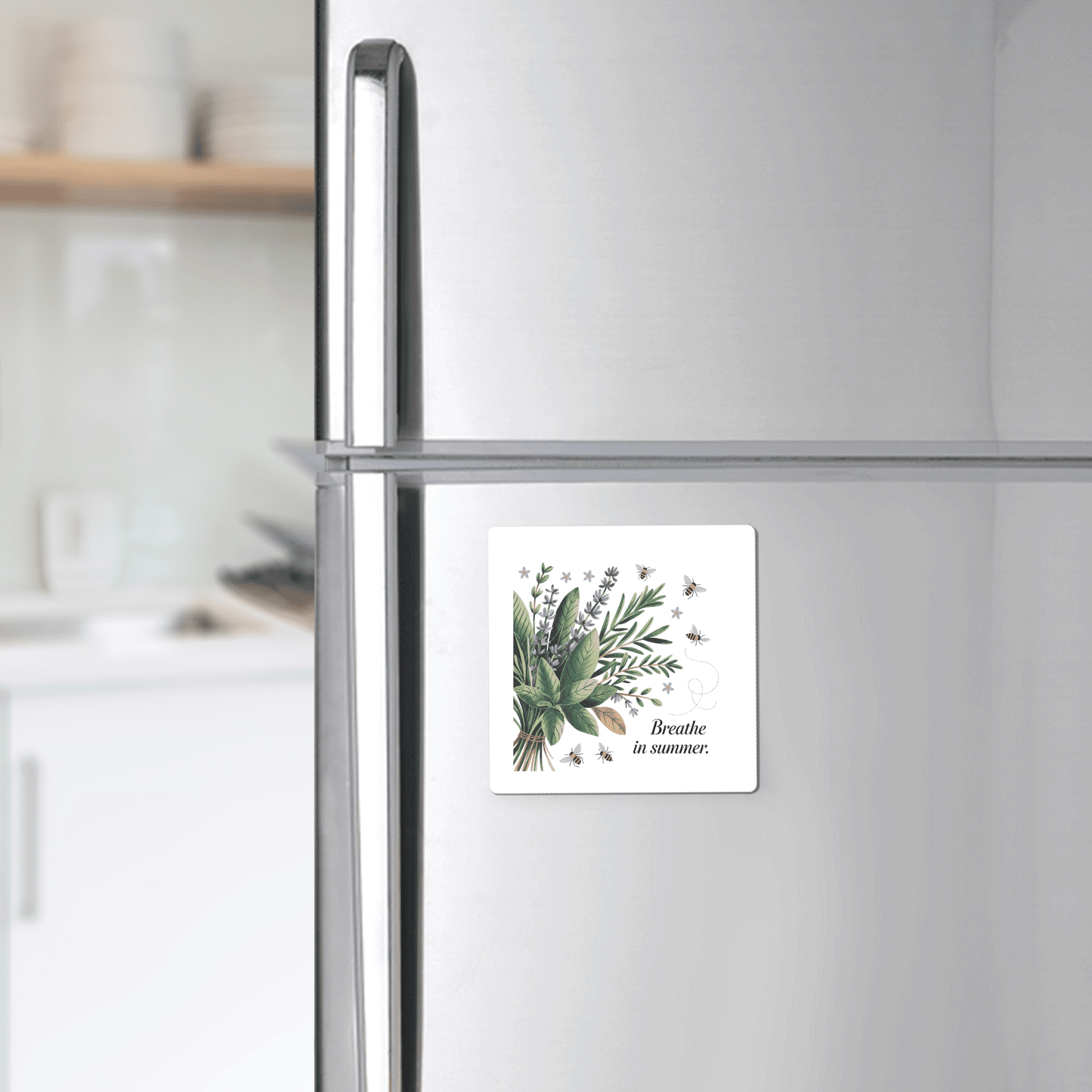 The Breathe in Summer Magnet – Botanical Calm & Gentle Bees by Mirabilia Boutique, featuring green leaves, purple flowers, bees, and the text "Breathe in summer," is displayed on a stainless steel fridge in a modern kitchen.