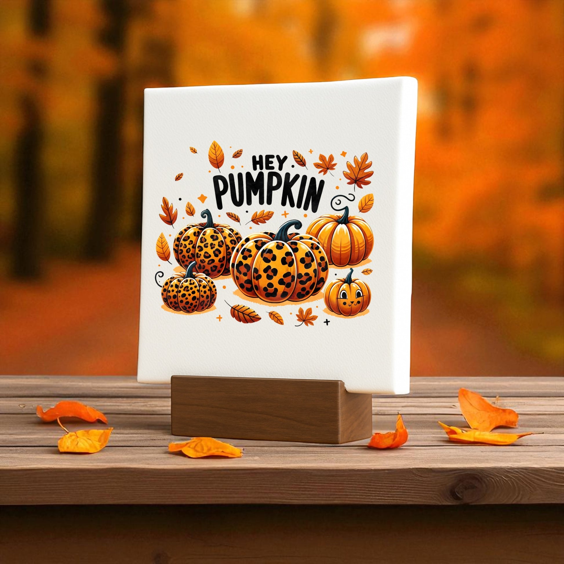 The Hey Pumpkin Mini Sign by Mirabilia Boutique features leopard-print pumpkins and autumn leaves on a wooden stand, perfect for cozy fall decor. This Leopard Pumpkin Canvas brings seasonal charm to any space.