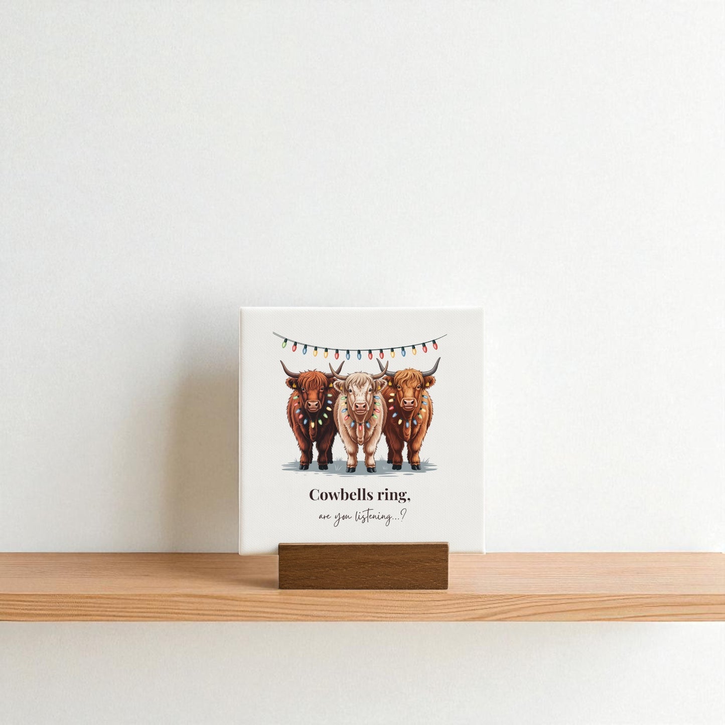 The Highland Cow Christmas Mini Sign by Mirabilia Boutique features three cows under festive lights on a 4x4 square, perfect for rustic farmhouse holiday decor. It reads: "Cowbells ring, are you listening?.