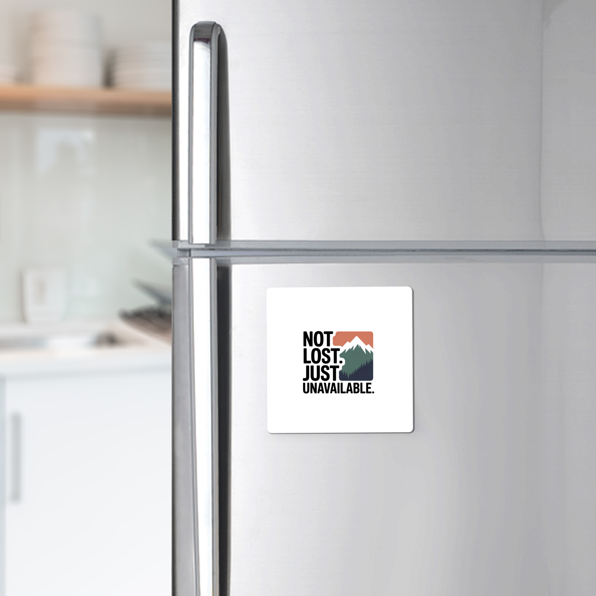 The Not Lost Just Unavailable Adventure Magnet by Mirabilia Boutique features a mountain graphic and the phrase "NOT LOST. JUST UNAVAILABLE."—a unique outdoor gift for adventurers, shown on a stainless steel fridge with a blurred kitchen in the background.