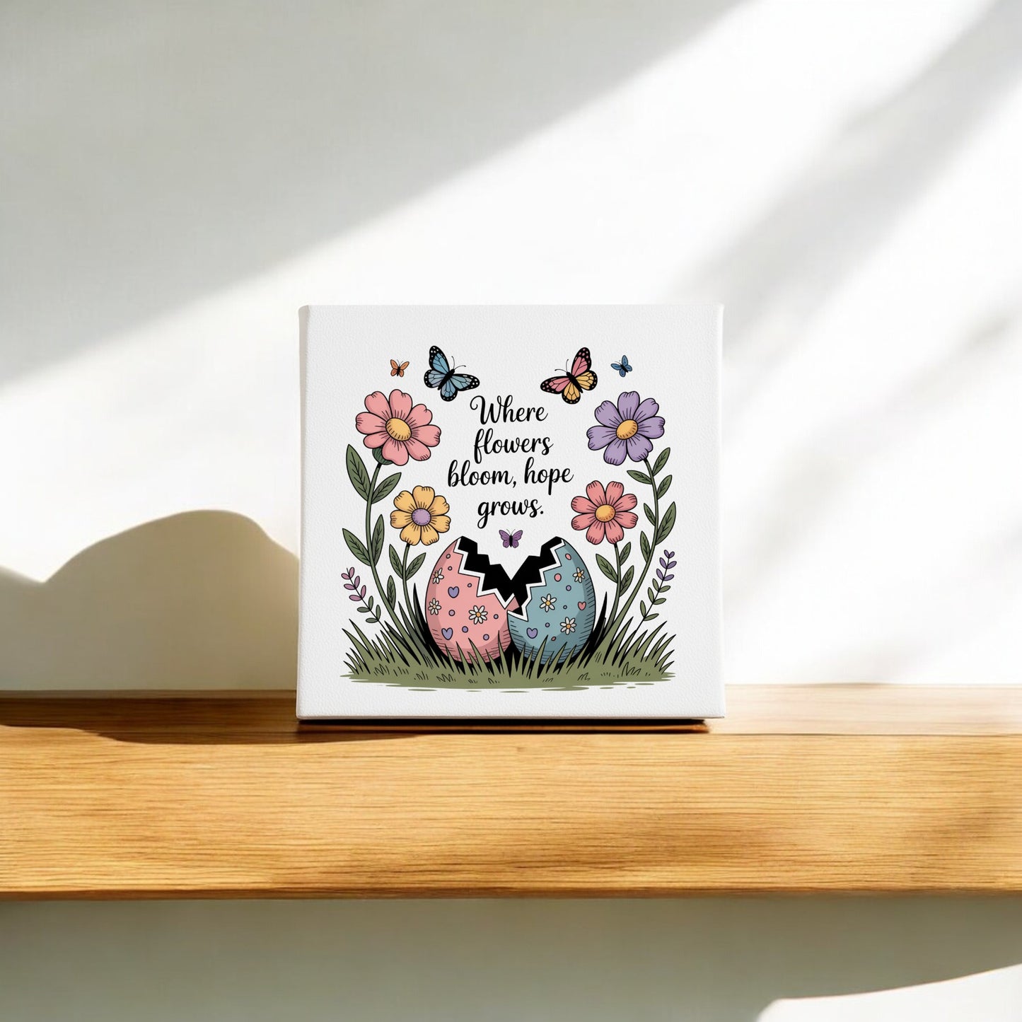 The Mirabilia Boutique "Where Flowers Bloom, Hope Grows" 8x8 Spring Canvas features vibrant flowers, butterflies, and a patterned egg—perfect Easter or spring decor to brighten any space.
