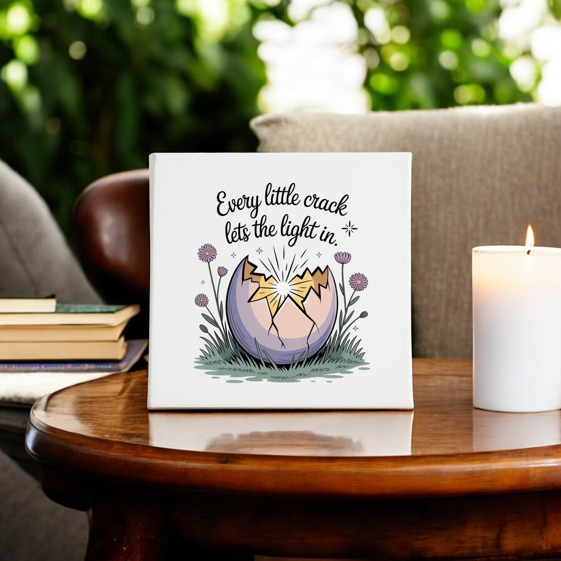 The Every Little Crack Lets the Light In Canvas Art by Mirabilia Boutique features a cracked egg glowing with light and surrounded by flowers, with the inspirational quote, perfect for wall decor. Lit candle, books, and plants add cozy charm to the scene.