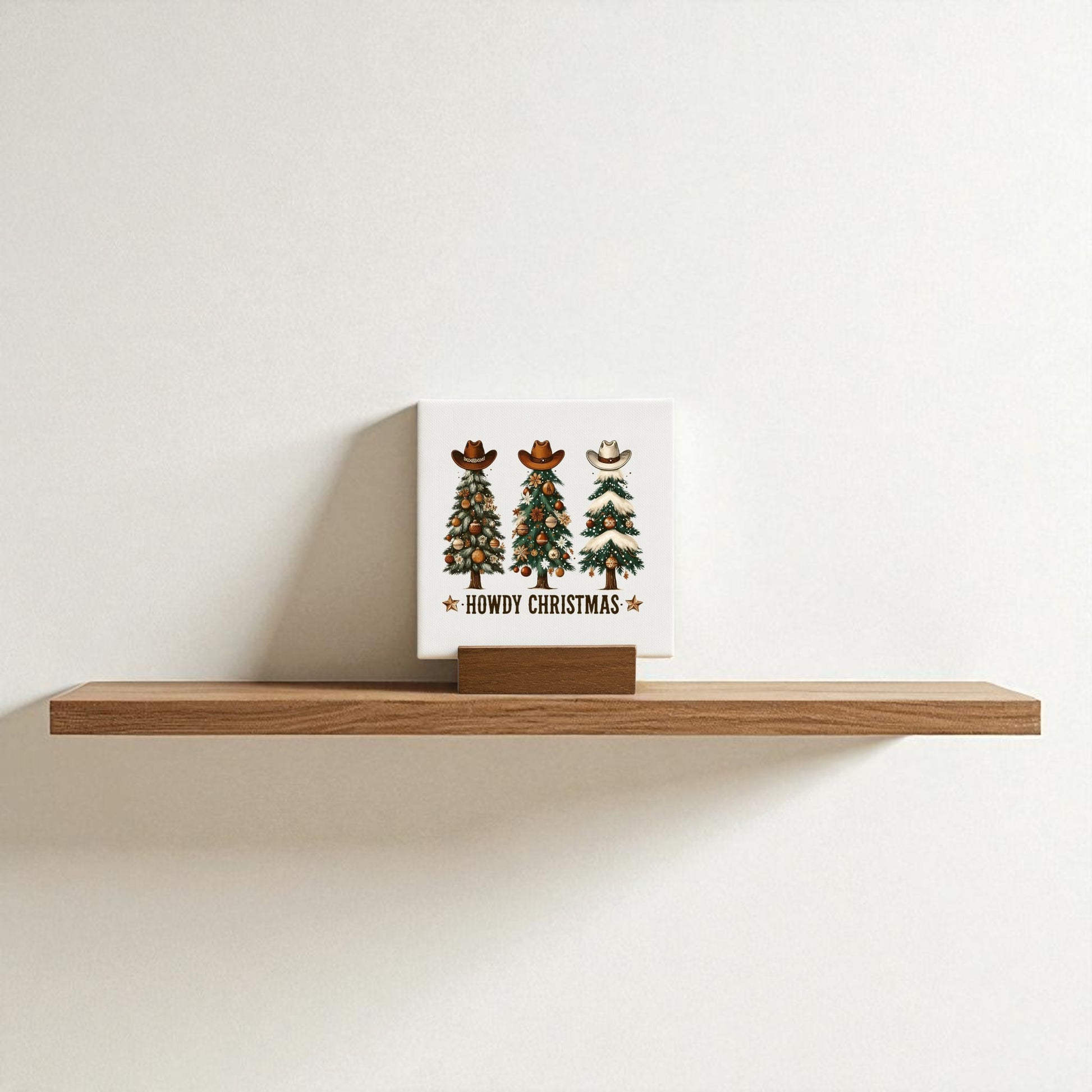 The Howdy Christmas Mini Sign by Mirabilia Boutique features three cowboy hat-topped Christmas trees and "Howdy Christmas" text, perfect as Western holiday shelf decor against a plain white wall.