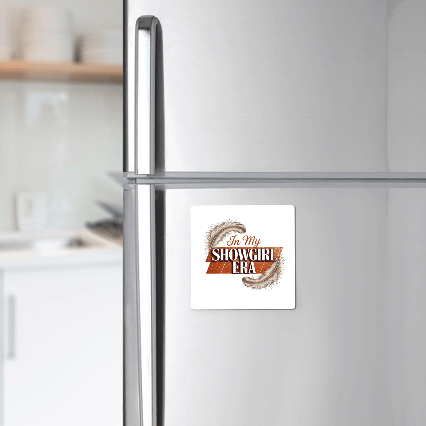 A silver refrigerator displays the Mirabilia Boutique "In My Showgirl Era Magnet | Glitter Vibes"—a fun fridge decor piece with feather accents and glam text, perfect for adding standout style to any modern kitchen.