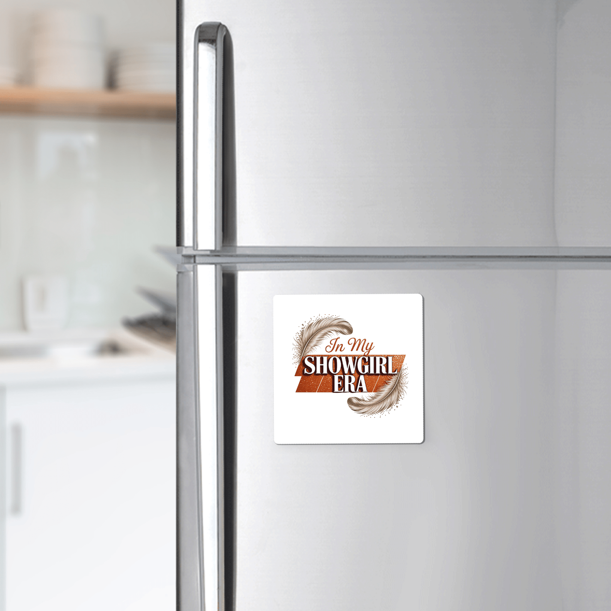 A silver refrigerator displays the Mirabilia Boutique "In My Showgirl Era Magnet | Glitter Vibes"—a fun fridge decor piece with feather accents and glam text, perfect for adding standout style to any modern kitchen.