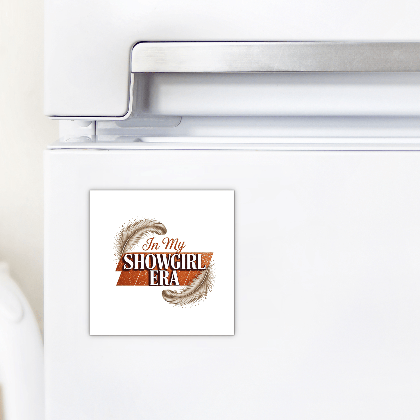 The "In My Showgirl Era Magnet" by Mirabilia Boutique adds glitter vibes to any white fridge, featuring decorative text and feather accents—fun showgirl decor for your kitchen.