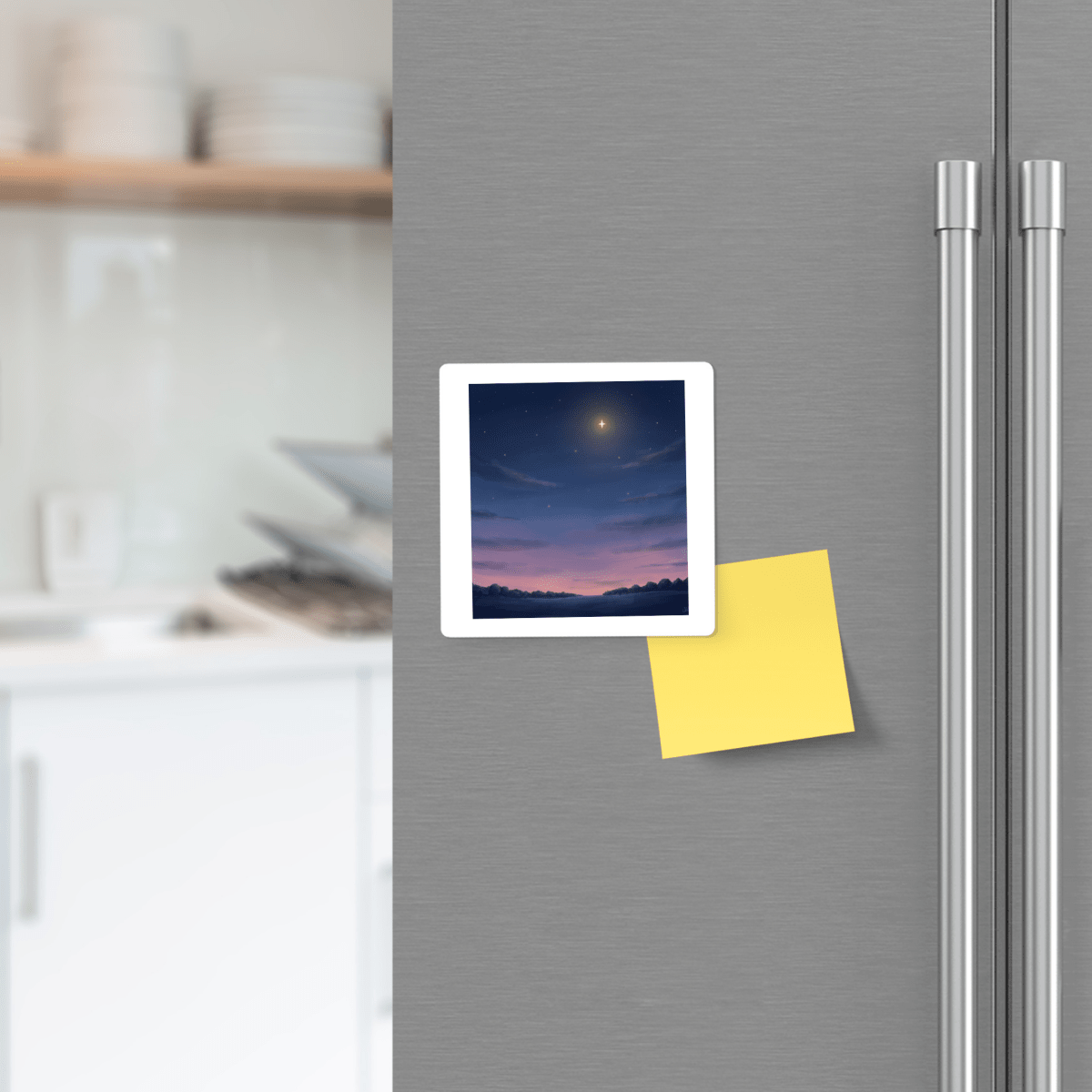 A stainless steel fridge adorned with the Look Up Celestial Magnet by Mirabilia Boutique, featuring a photo of a sunset sky, along with a yellow sticky note attached to the door. Kitchen shelves with dishes are seen in the background.
