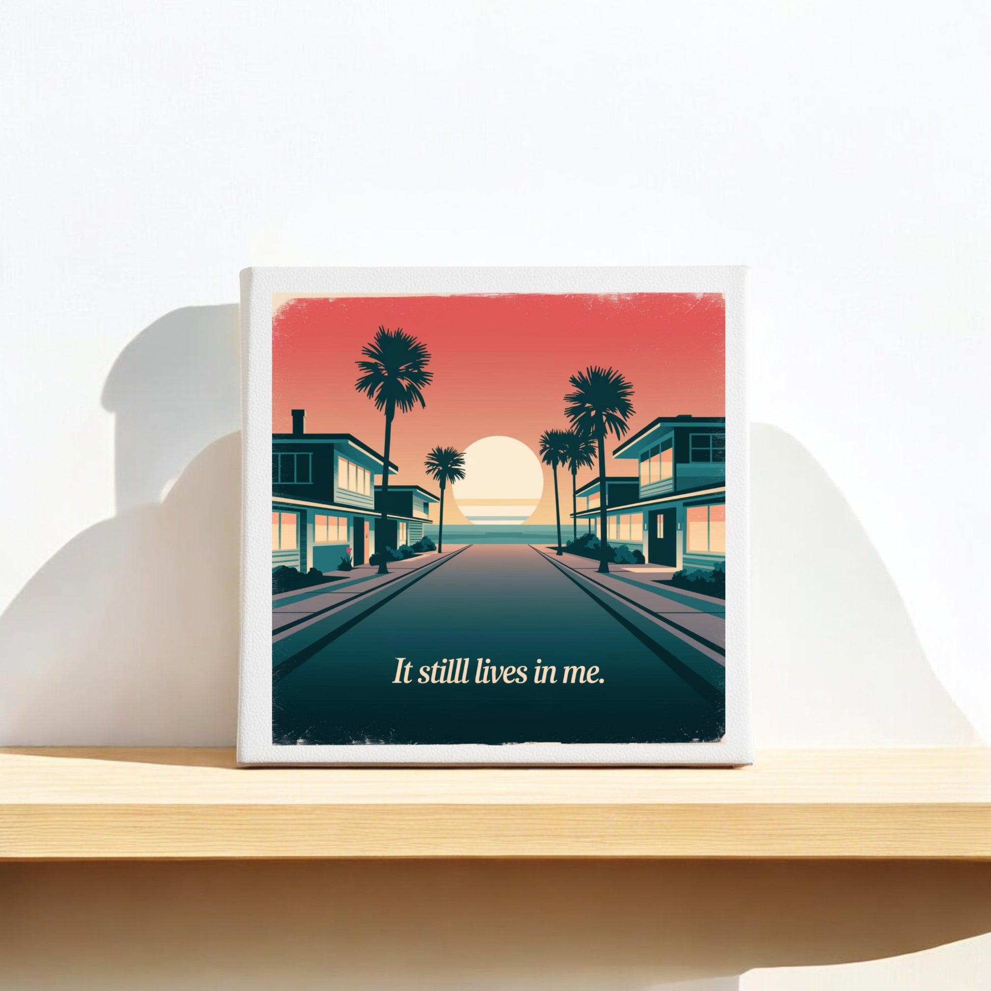 The "It Still Lives in Me Canvas – Retro Sunset Memory Art" by Mirabilia Boutique features a nostalgic sunset between palm-lined buildings with the phrase "It still lives in me," perfect for retro beach decor on any shelf or wall.
