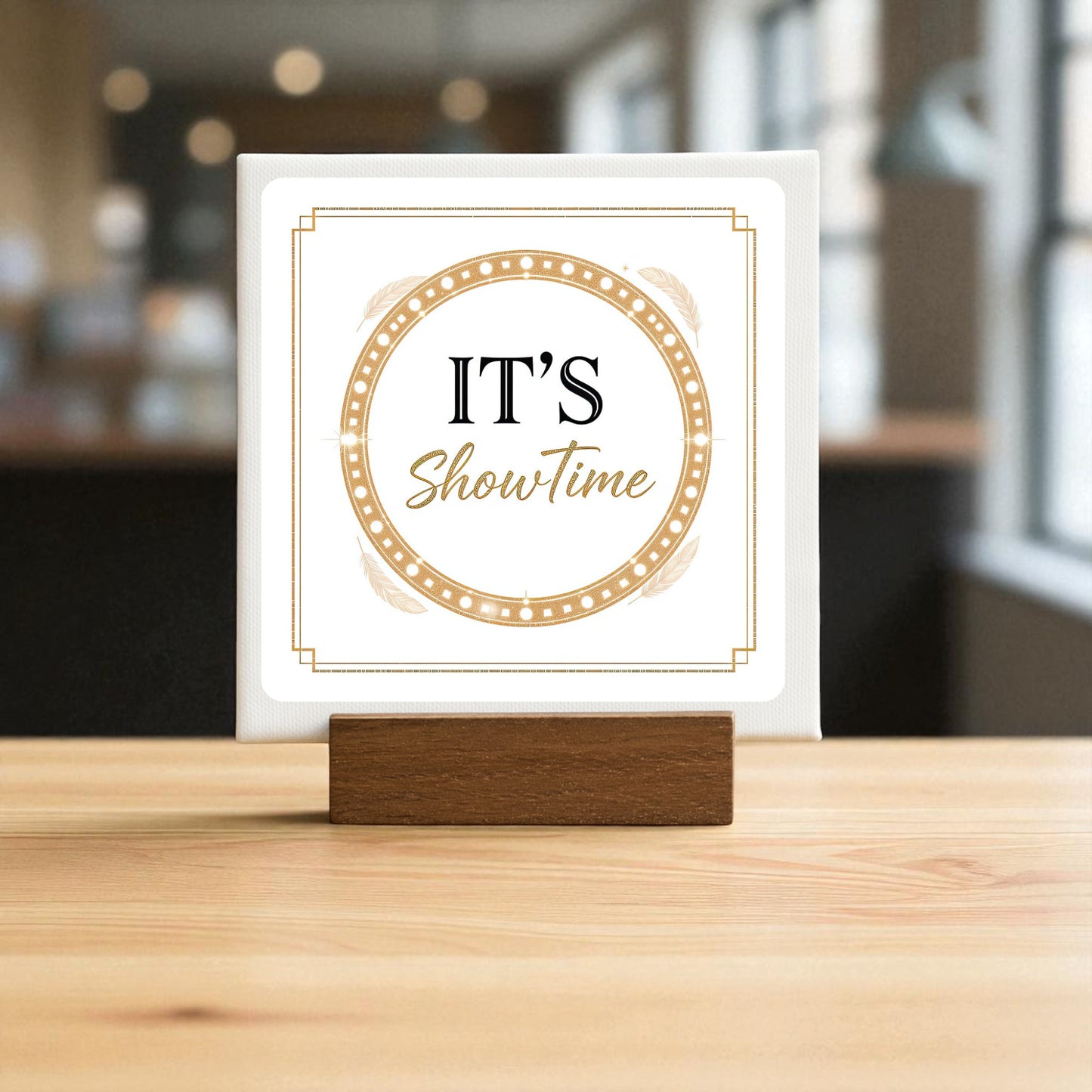 The “It’s Showtime Mini Sign” by Mirabilia Boutique features the phrase in stylish black and gold within a circular border, set on a wooden stand—perfect as glamorous stage decor or a chic motivational accent for your desk.