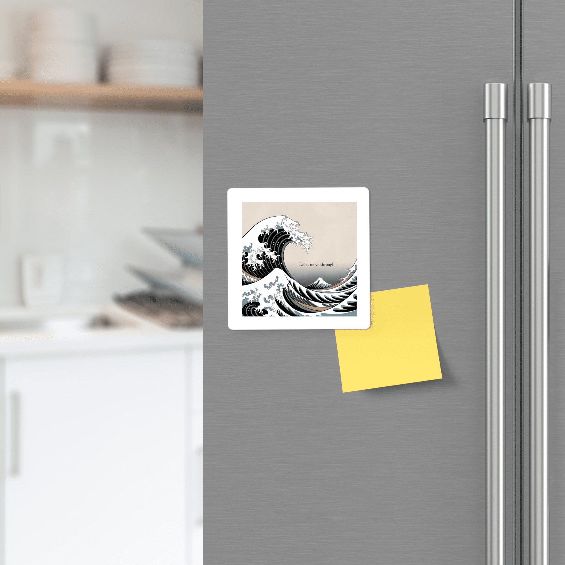The Let It Move Through Magnet – Storm & Stillness Quote by Mirabilia Boutique, featuring an ocean wave design and an inspiring message, is displayed on a stainless steel fridge next to a blank yellow sticky note in a modern kitchen.