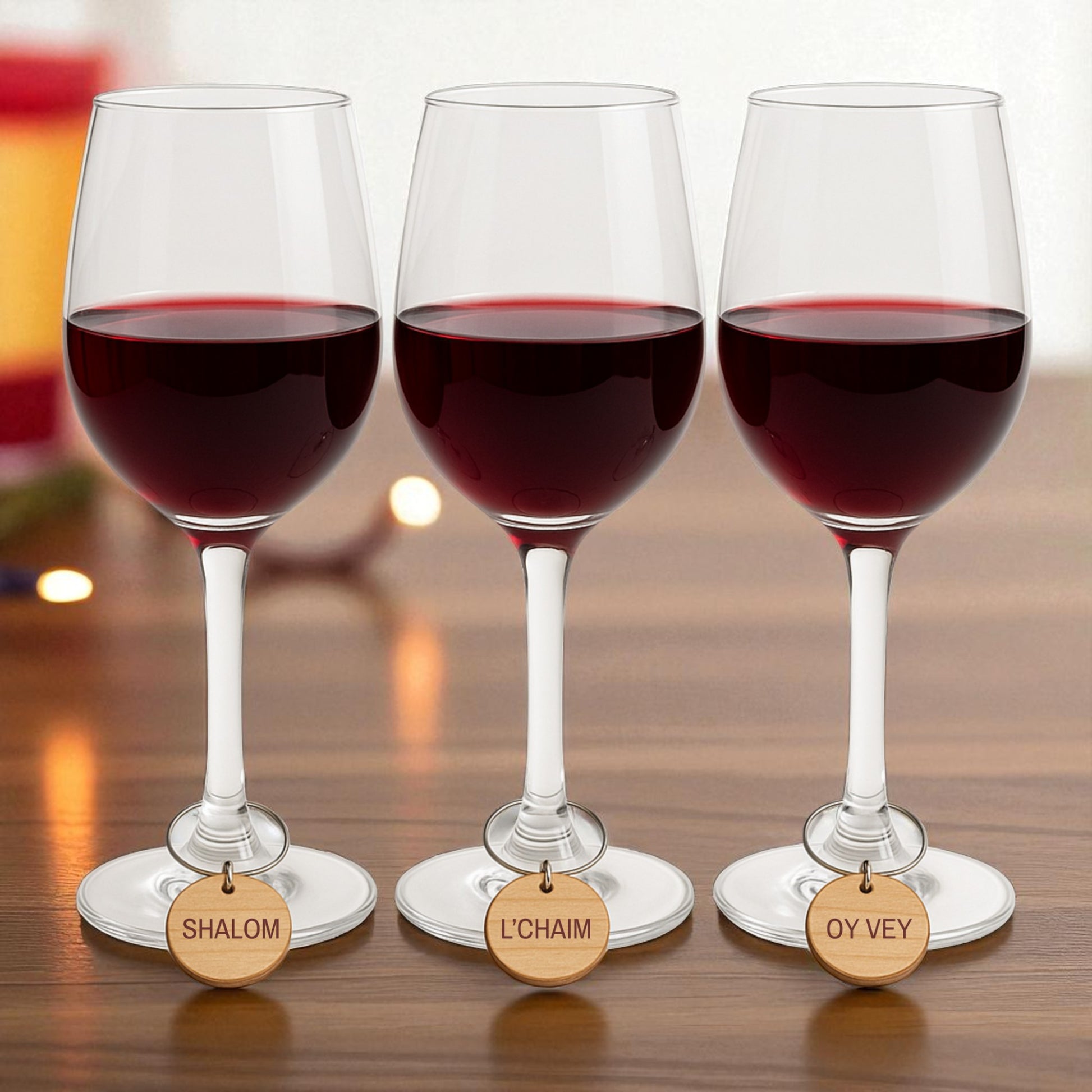 Mirabilia Boutique’s Jewish Wine Charms | Hanukkah Wine Glass Markers Set of 8—featuring “SHALOM,” “L’CHAIM,” and “OY VEY”—decorate red wine glasses on a wooden table, glowing lights behind them, perfect for festive Jewish holiday gifts.