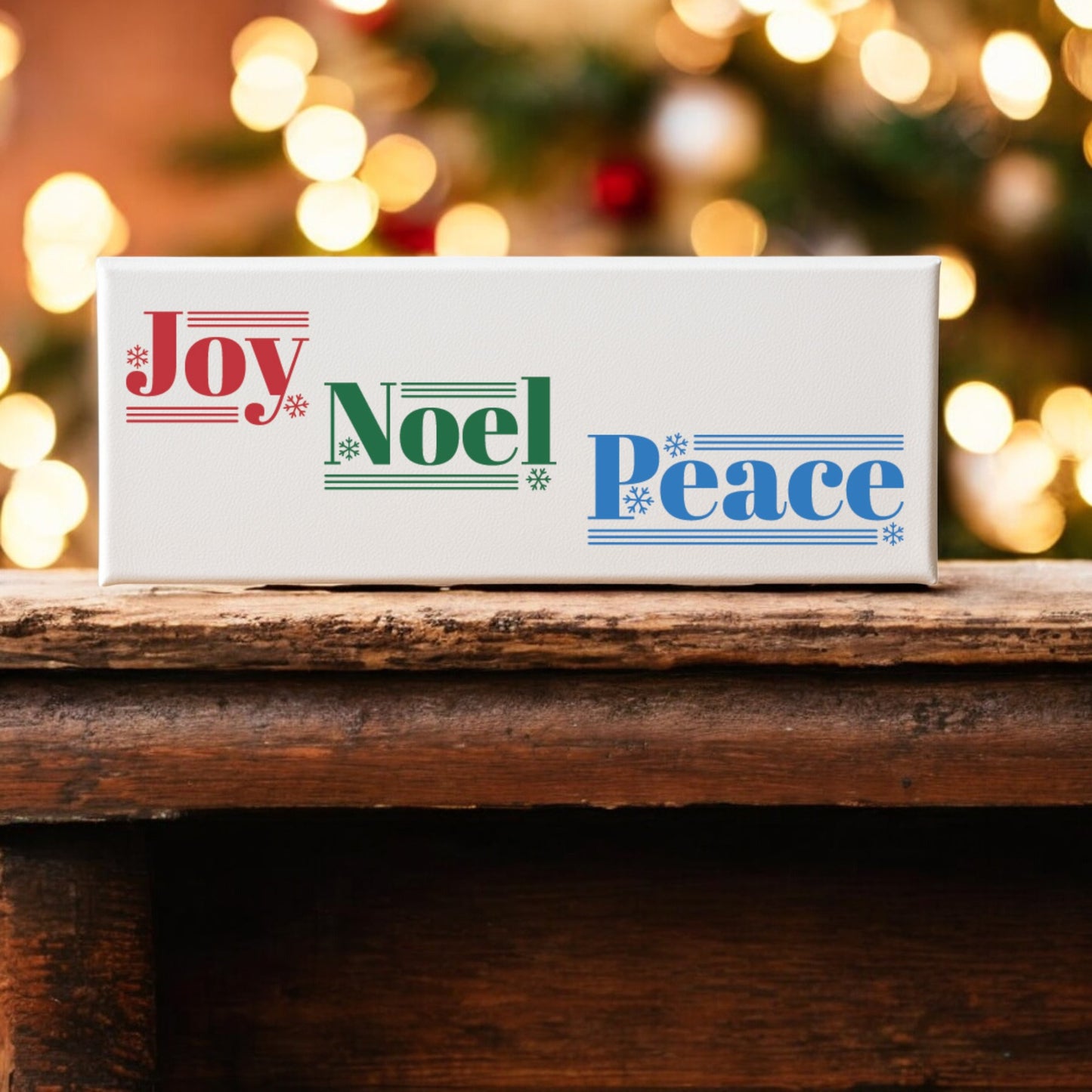 The Mirabilia Boutique Joy Noel Peace Christmas Sign, a 4x12 canvas shelf sitter, displays “Joy” in red, “Noel” in green, and “Peace” in blue with snowflakes—perfect festive decor for your shelf or mantle.