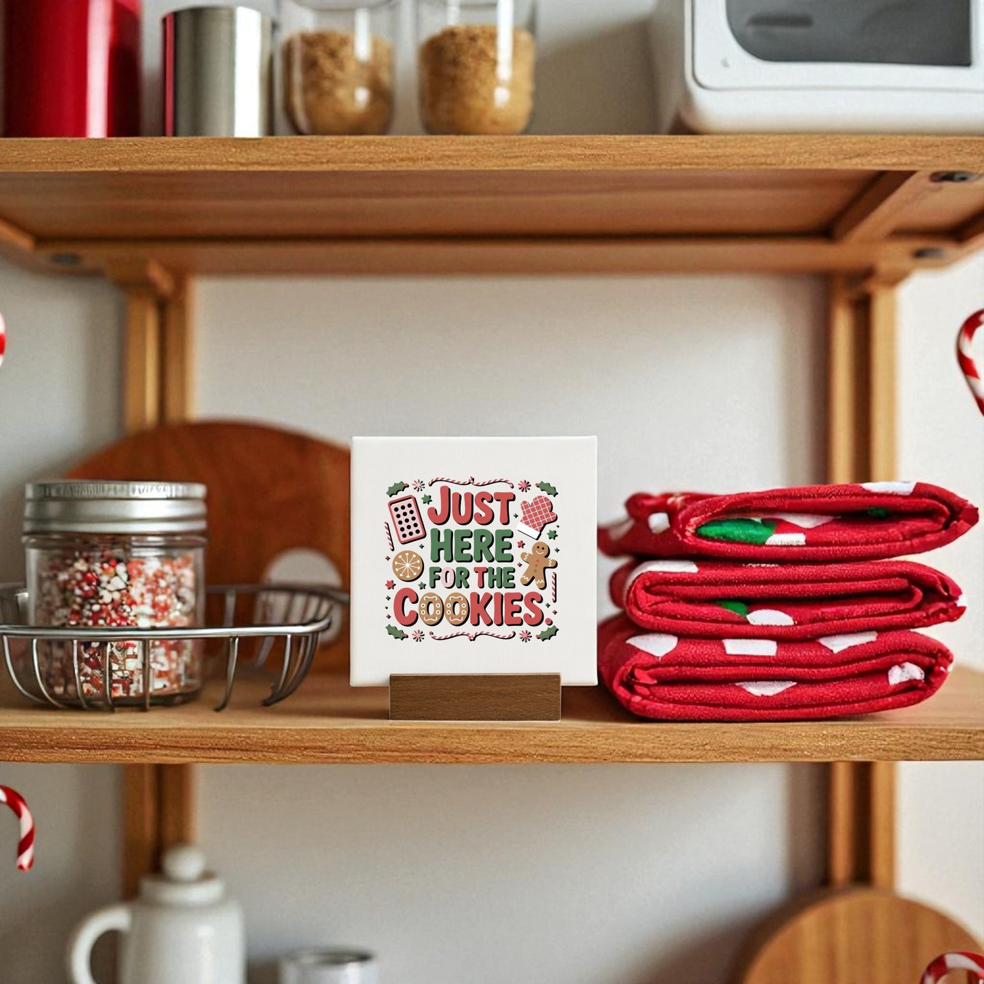 A cozy kitchen shelf showcases the Mirabilia Boutique “Just Here for the Cookies Mini Sign” beside red and white towels, holiday sprinkles, and festive Christmas cookie decor for a charming seasonal touch.