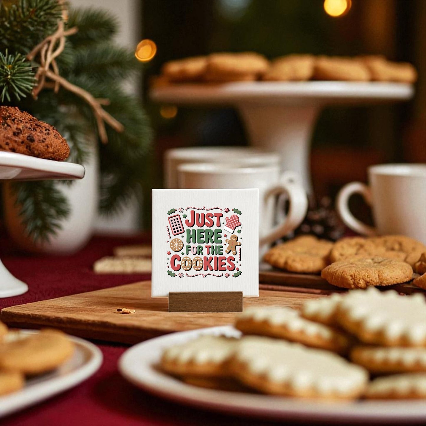 A festive table features the Mirabilia Boutique “Just Here for the Cookies Mini Sign” alongside cookies and cups, surrounded by Christmas cookie decor and warm lighting. The cute sign adds charm to your holiday shelf decor.