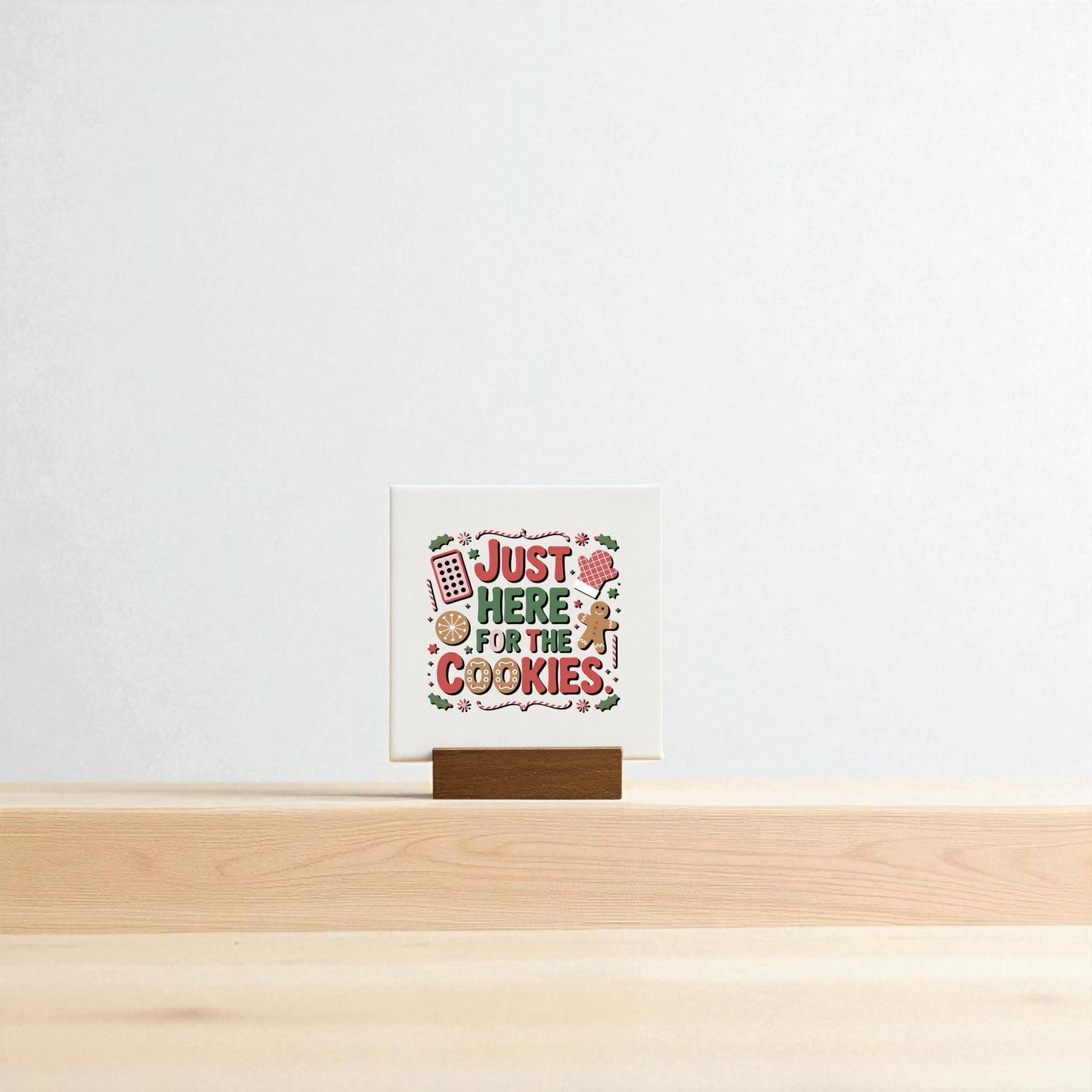 The "Just Here for the Cookies Mini Sign" by Mirabilia Boutique features playful lettering and baking illustrations on a wooden stand, making it a cute Christmas shelf decor or cookie-themed gift. Set against a plain light background.