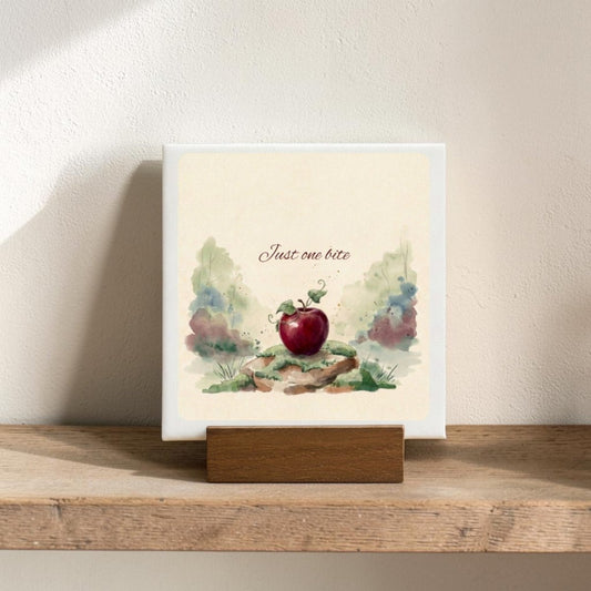 The Just One Bite Mini Canvas Sign by Mirabilia Boutique features a red apple with green leaves and the phrase "Just one bite" above it, surrounded by watercolor-style foliage on a wooden shelf—making it a charming fairy tale decor accent for any woodland-inspired space.