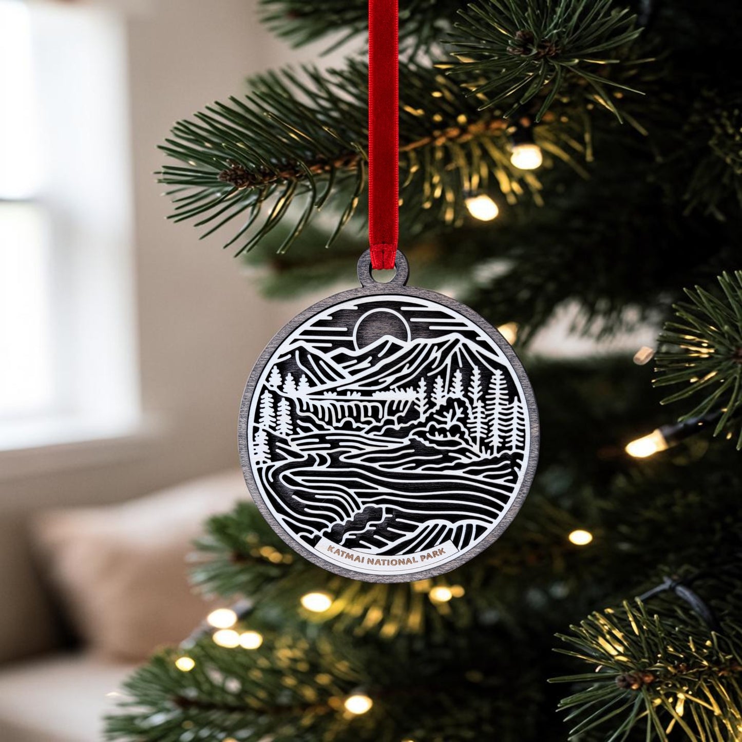 A beautifully handcrafted Katmai National Park Line Art Christmas Ornament by Mirabilia Boutique hangs from a red ribbon on a Christmas tree adorned with twinkling lights, capturing the wild spirit of Alaska brown bears.