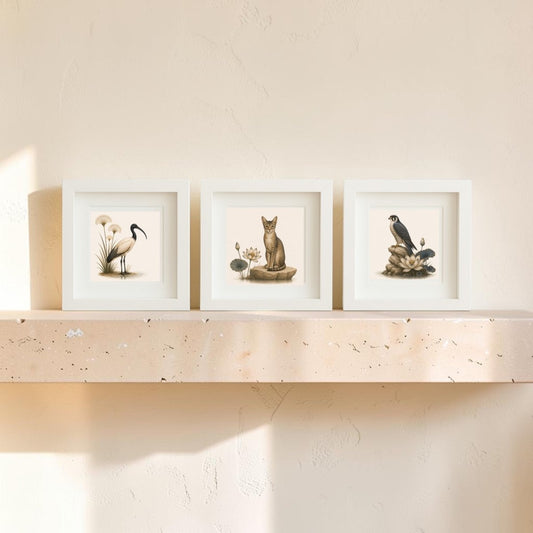 Three framed canvas artworks—a crane, a cat, and a penguin—are displayed side by side on a beige stone shelf against a light-colored wall bathed in soft natural light. Part of the “Keepers of the Nile” collection from Mirabilia Boutique, these pieces subtly draw on Nile wildlife art for inspiration.