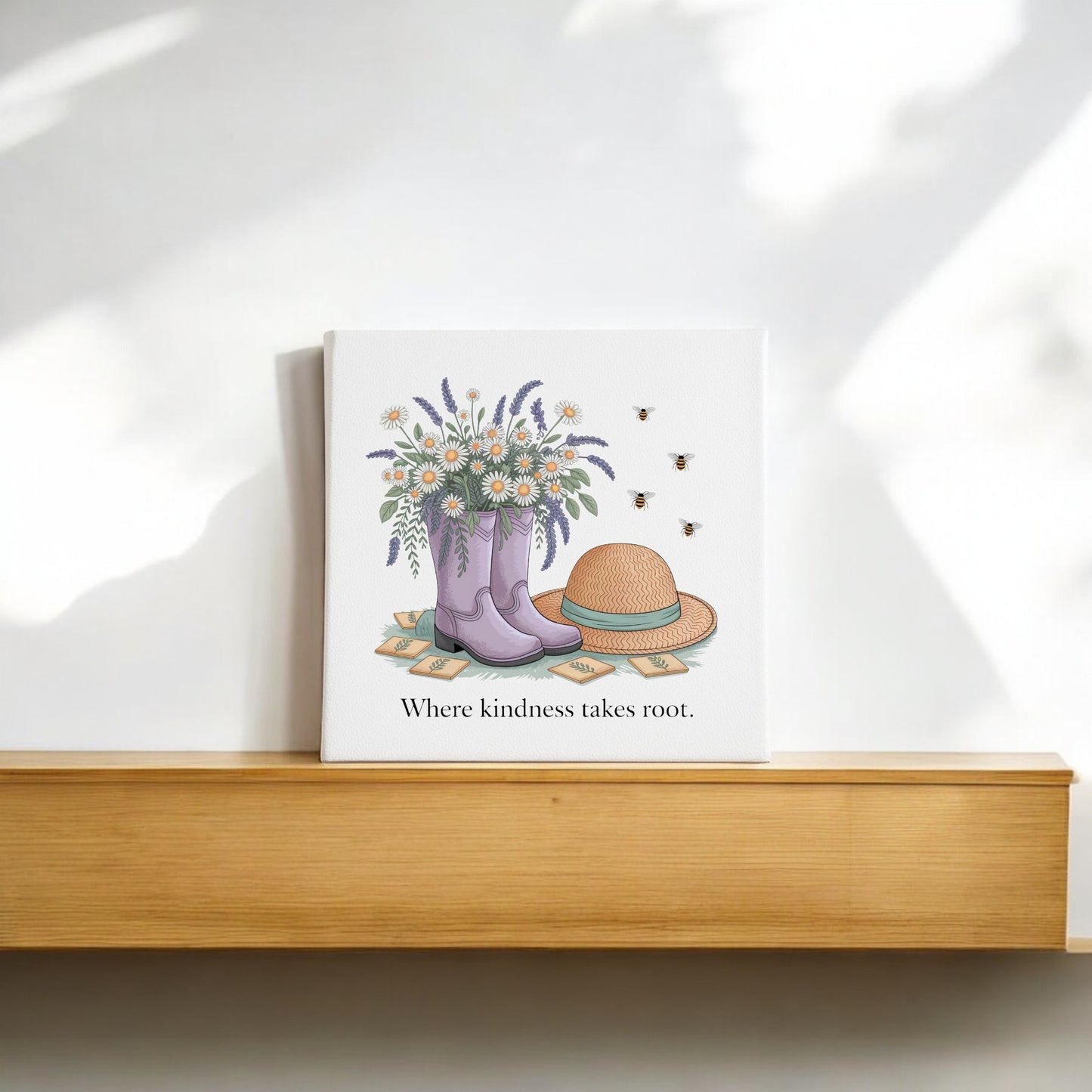 The Kindness Takes Root Canvas by Mirabilia Boutique features purple rain boots with wildflowers, a straw hat, and bees. With the phrase “Where kindness takes root,” this garden-inspired wall art adds spring warmth to your décor.