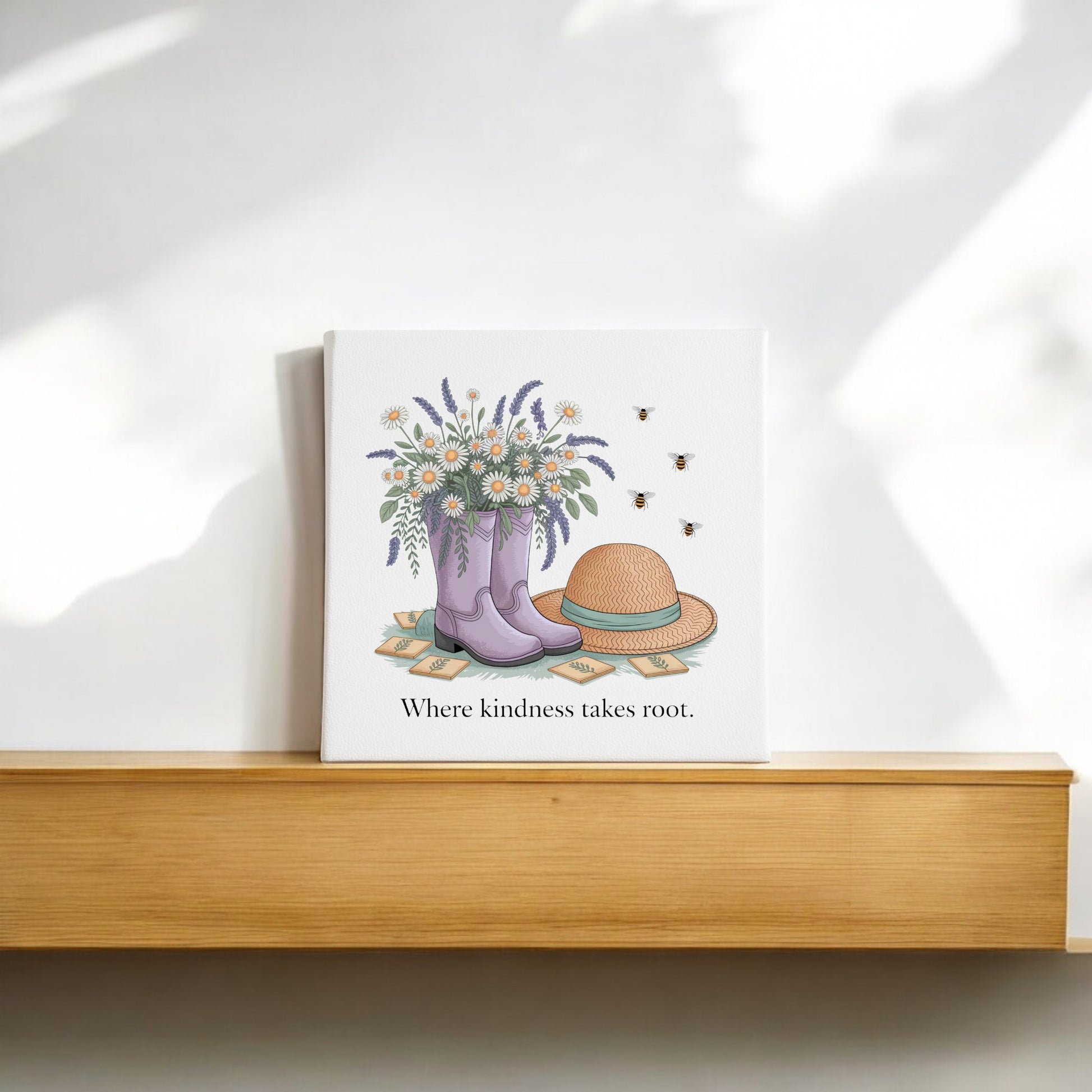The Kindness Takes Root Canvas by Mirabilia Boutique features purple rain boots with wildflowers, a straw hat, and bees. With the phrase “Where kindness takes root,” this garden-inspired wall art adds spring warmth to your décor.