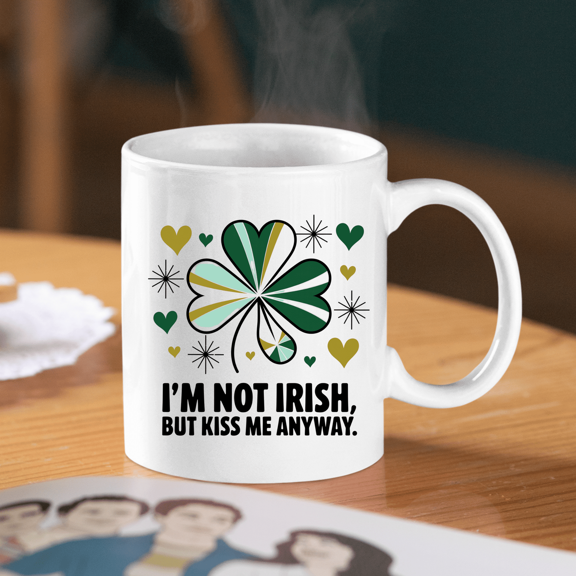 The Kiss Me Anyway Mug – St. Patrick’s Day Charm by Mirabilia Boutique sits on a wooden table, decorated with a green and yellow shamrock, hearts, stars, and the phrase “I’M NOT IRISH, BUT KISS ME ANYWAY.” Steam rises from the festive mug.