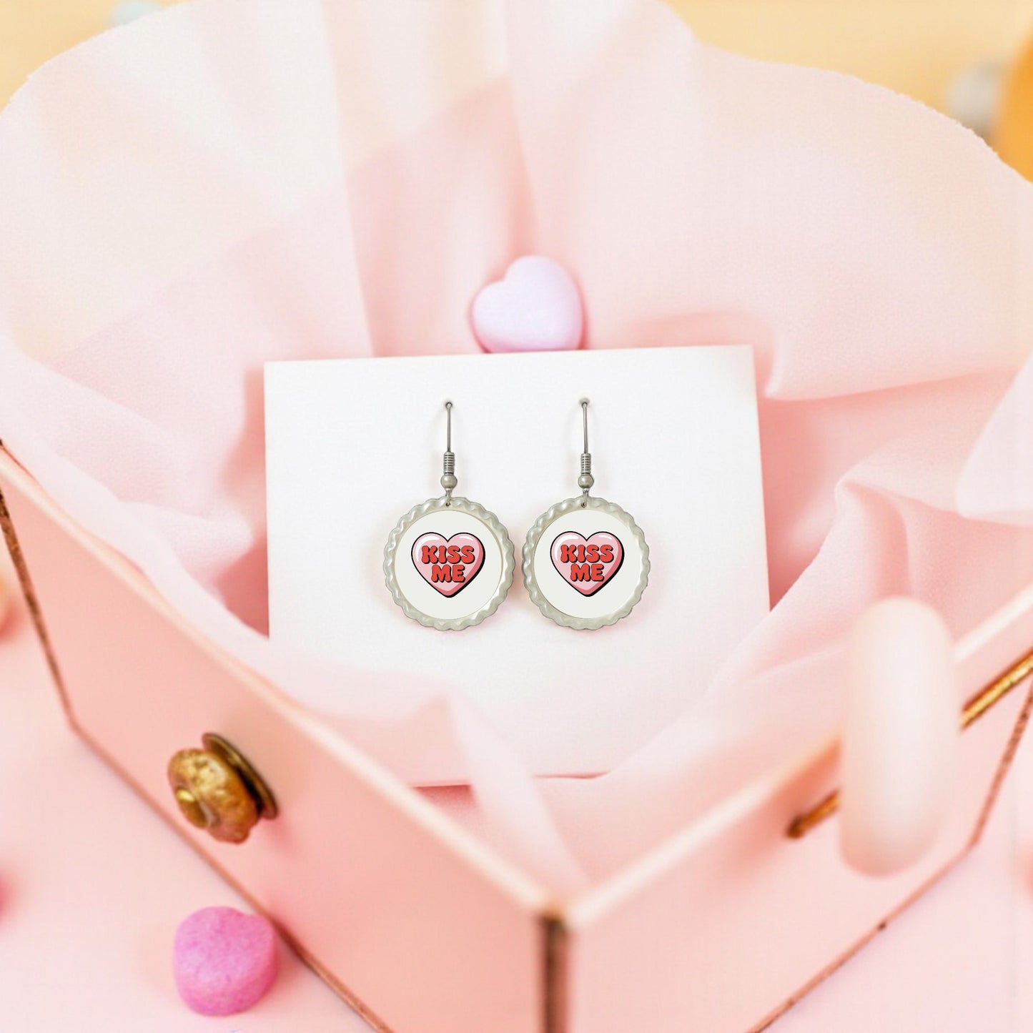 The Kiss Me Heart Earrings by Mirabilia Boutique feature “KISS ME” inside pink hearts, presented on a white card in a pink heart jewelry box—an ideal Valentine’s Day gift for her.
