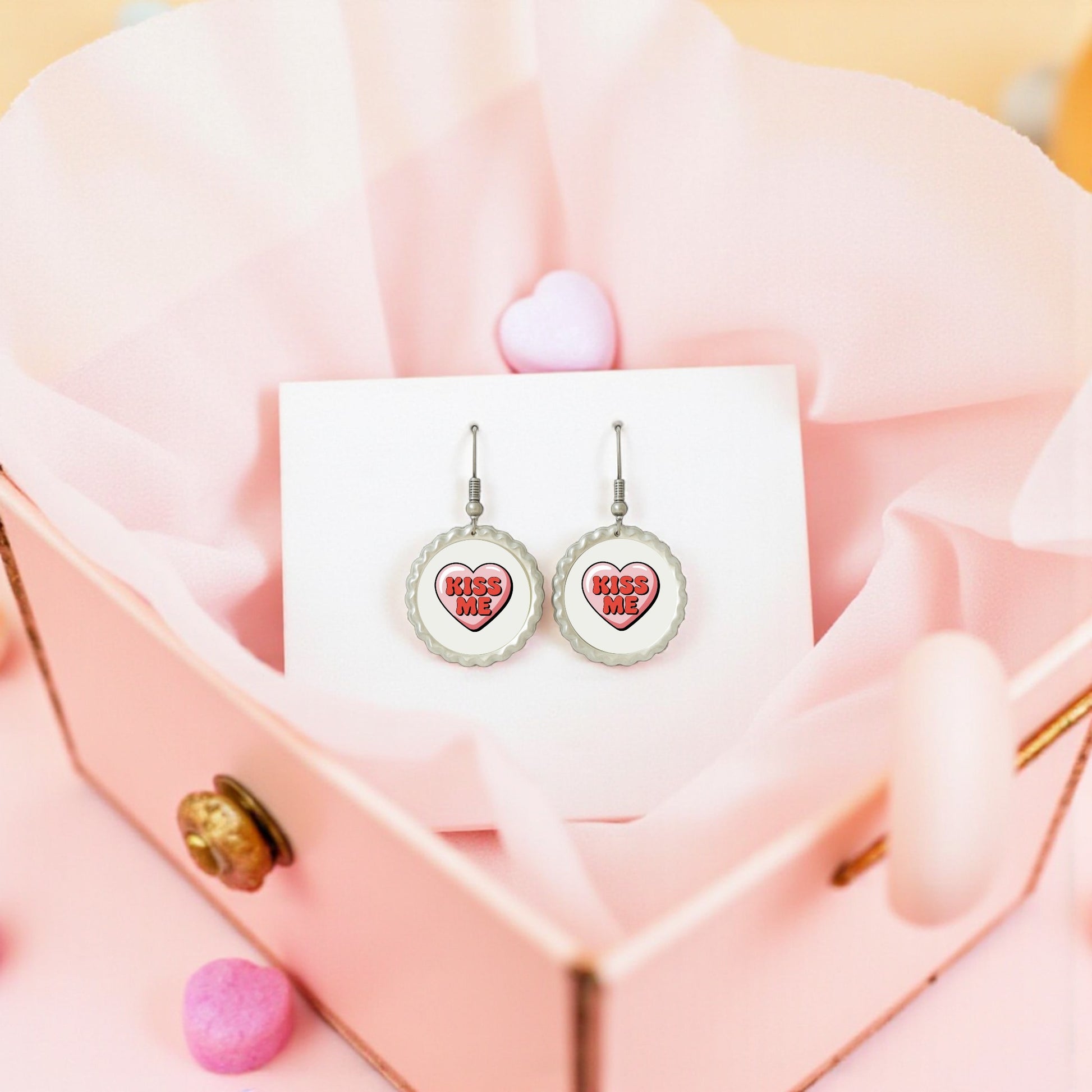 The Kiss Me Heart Earrings by Mirabilia Boutique feature “KISS ME” inside pink hearts, presented on a white card in a pink heart jewelry box—an ideal Valentine’s Day gift for her.