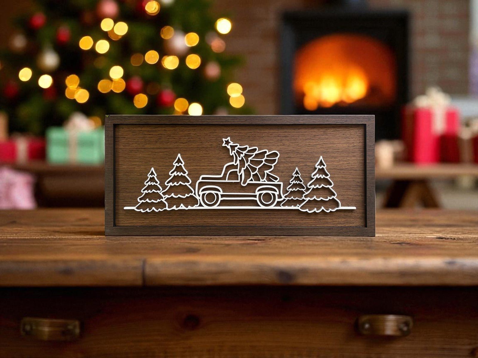 The Mirabilia Boutique Truck & Tree Laser Cut Christmas Sign (9x4 Rustic Wall Art) features a white outlined truck and tree among pines—perfect for modern farmhouse decor—displayed with a festive tree, fireplace, and gifts.