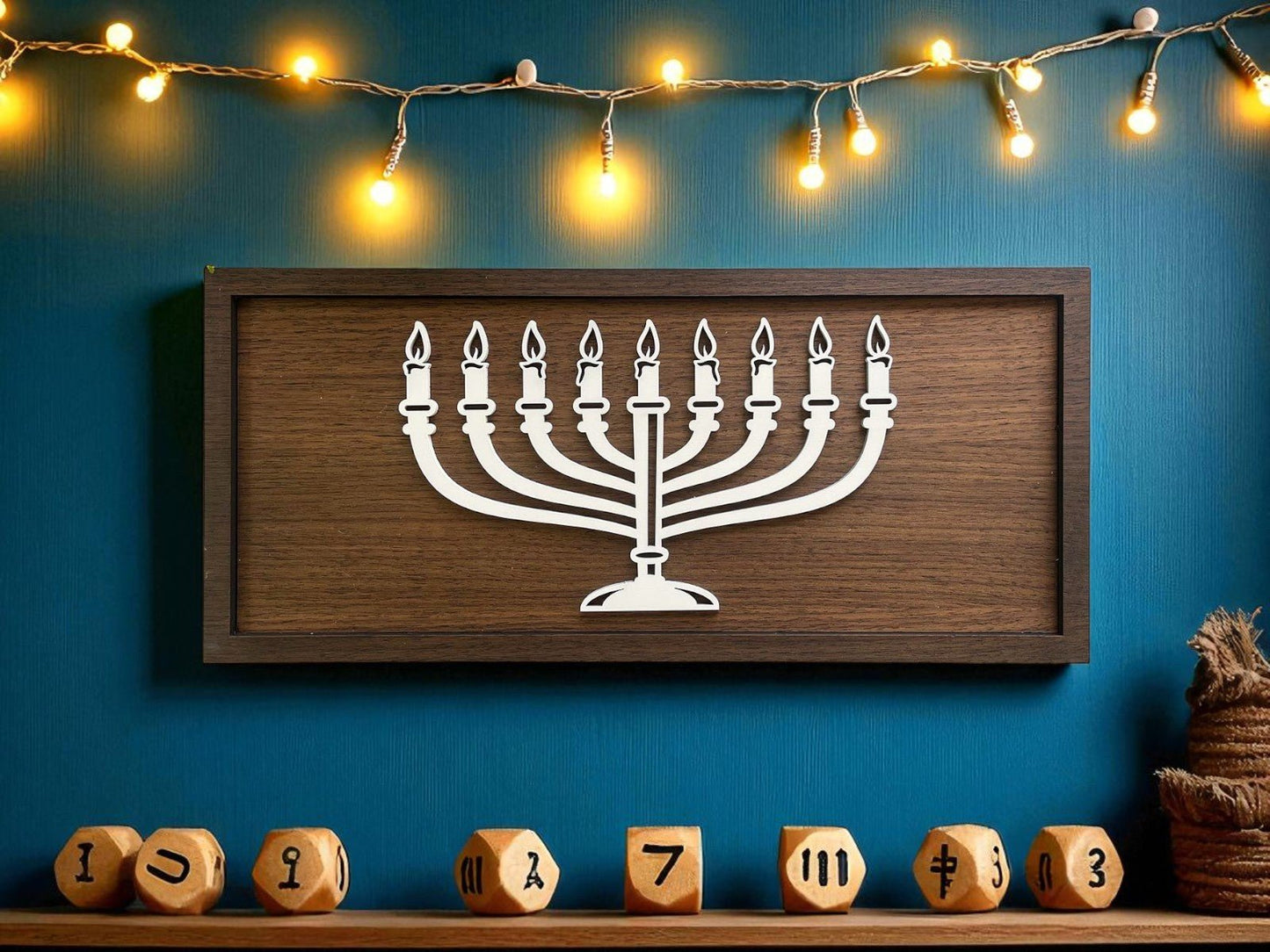 The 18x8 Modern Menorah Sign by Mirabilia Boutique hangs on a blue wall with string lights above. Wooden dreidels with Hebrew letters sit below, making for chic, minimalist Hanukkah decor.