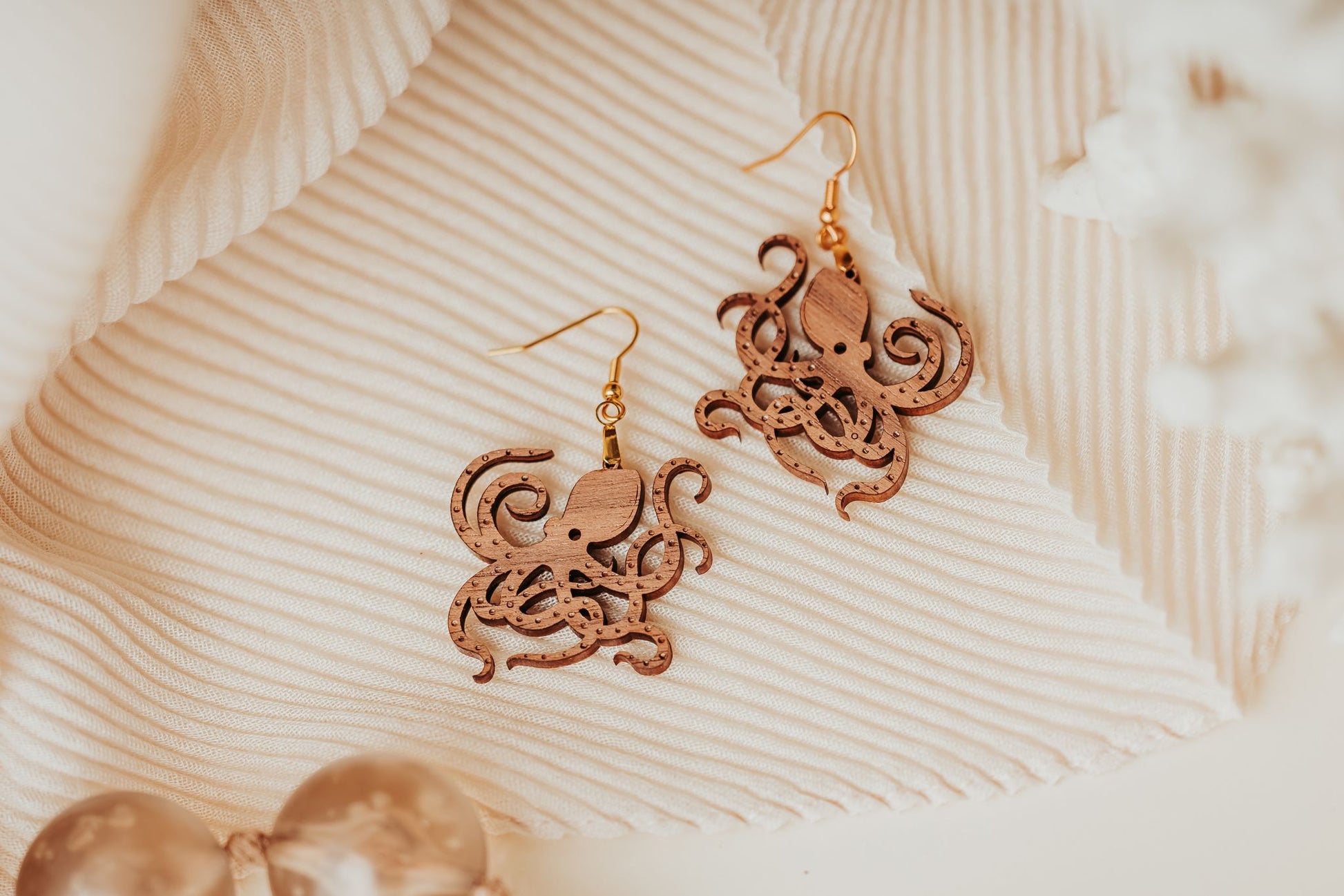 Mirabilia Boutique’s Octopus Earrings—laser cut wood ocean jewelry with gold hooks—make an elegant gift for nature or sea life lovers, beautifully displayed on cream fabric.