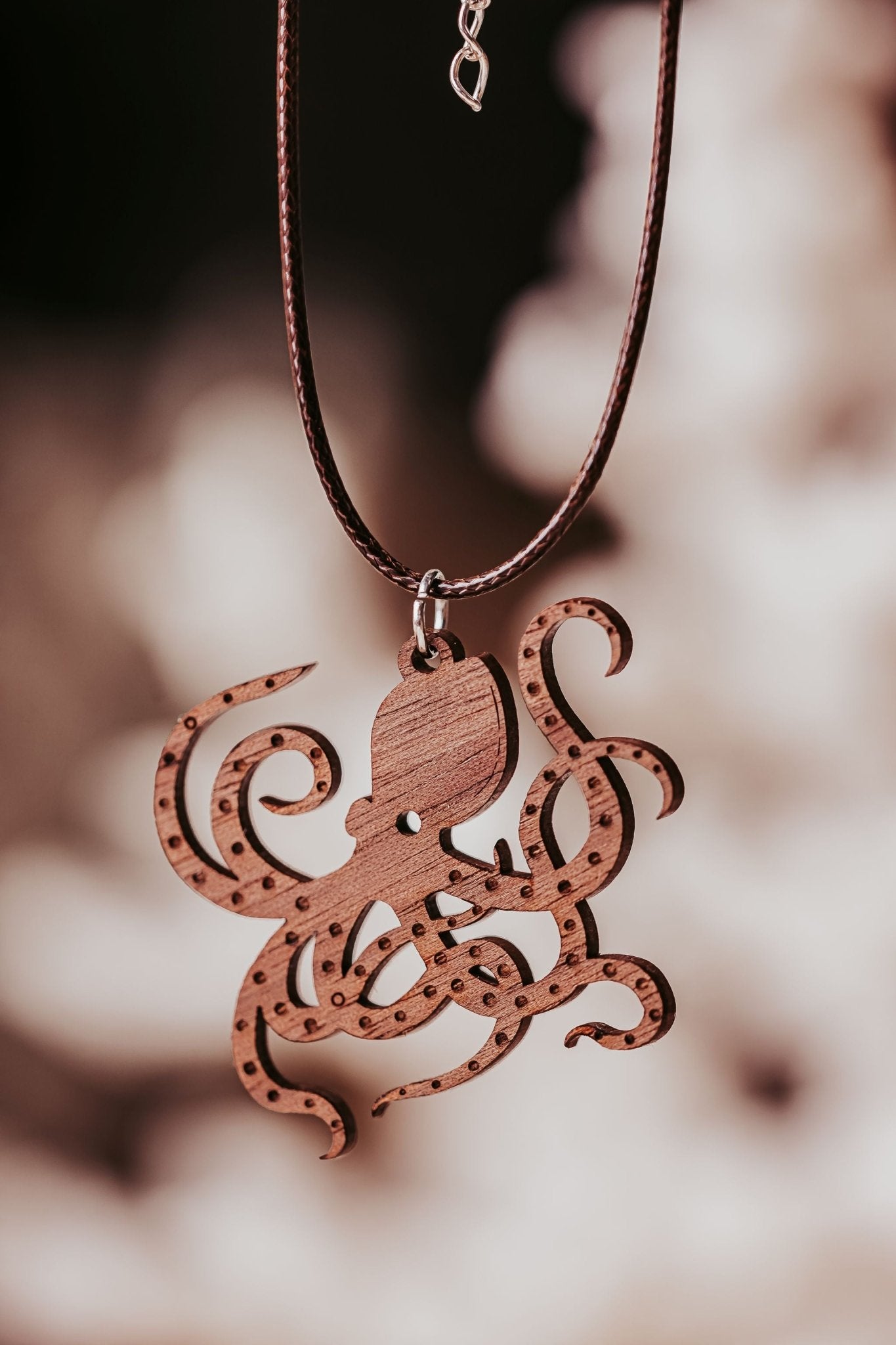 The Wooden Octopus Necklace by Mirabilia Boutique is a nautical pendant for ocean lovers, featuring an eco-friendly wood octopus on a brown cord, creating unique, ocean-inspired jewelry against a blurred background.