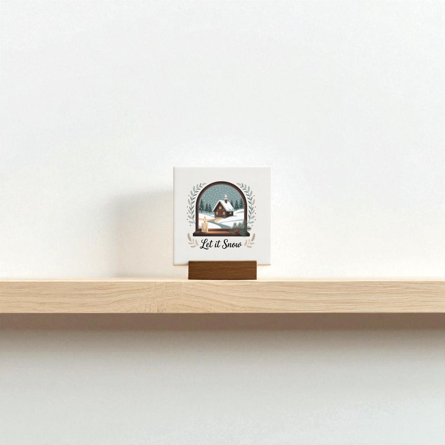 The Mirabilia Boutique Let It Snow Mini Sign, a 4x4 winter canvas with wood base, displays a snowy house and trees with "Let it Snow," creating charming seasonal decor on a plain white wall.
