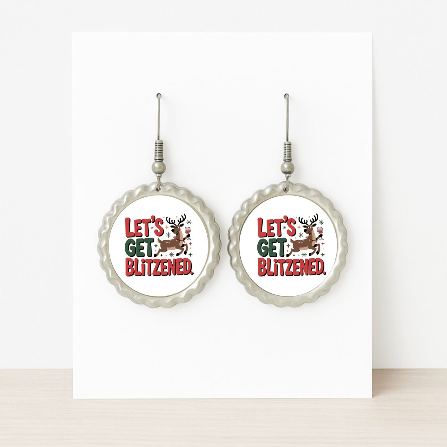 Mirabilia Boutique's "Let's Get Blitzened" round silver earrings feature a holiday reindeer and festive red & green text—funny Christmas earrings displayed on a white card, perfect for your next holiday party.