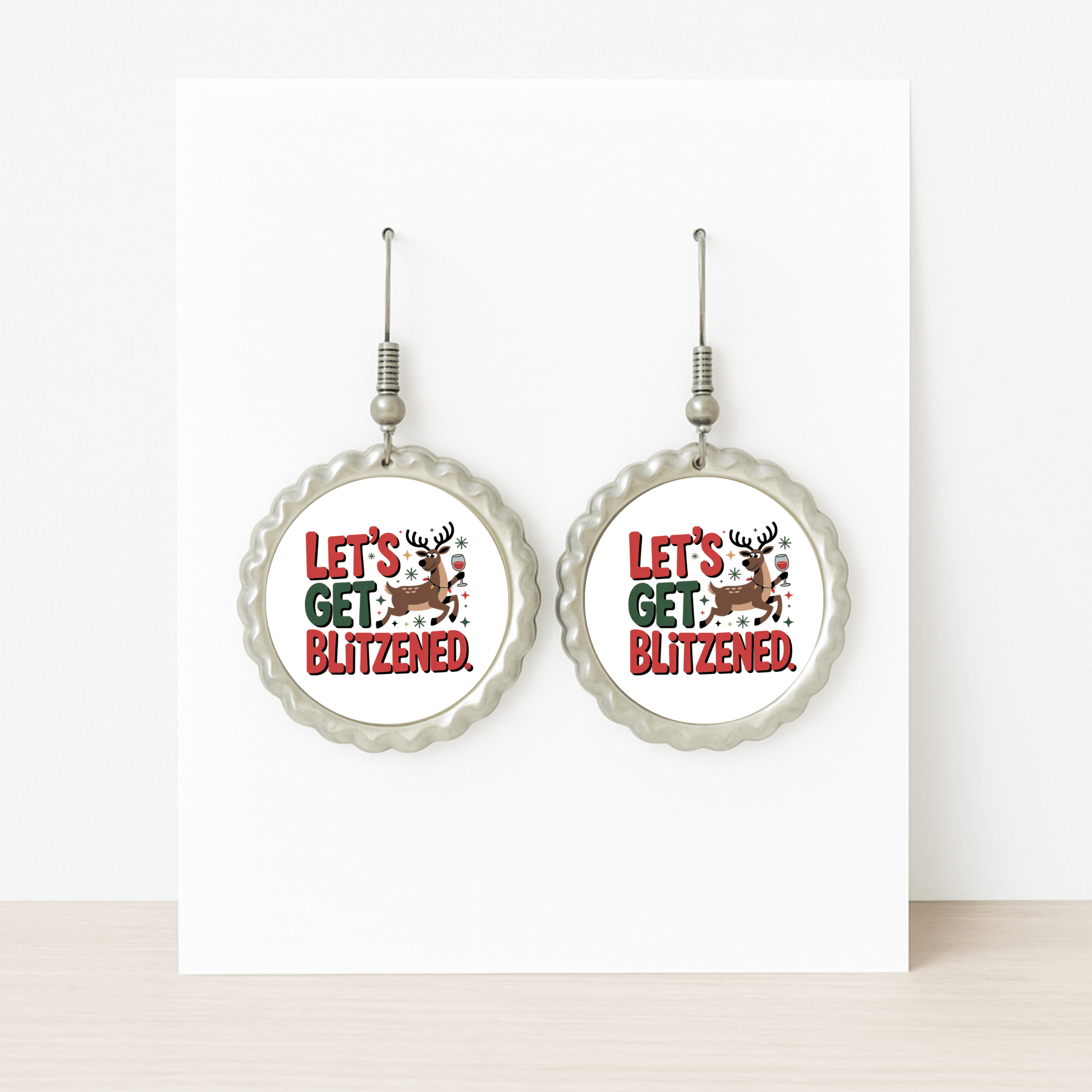 Mirabilia Boutique's "Let's Get Blitzened" round silver earrings feature a holiday reindeer and festive red & green text—funny Christmas earrings displayed on a white card, perfect for your next holiday party.