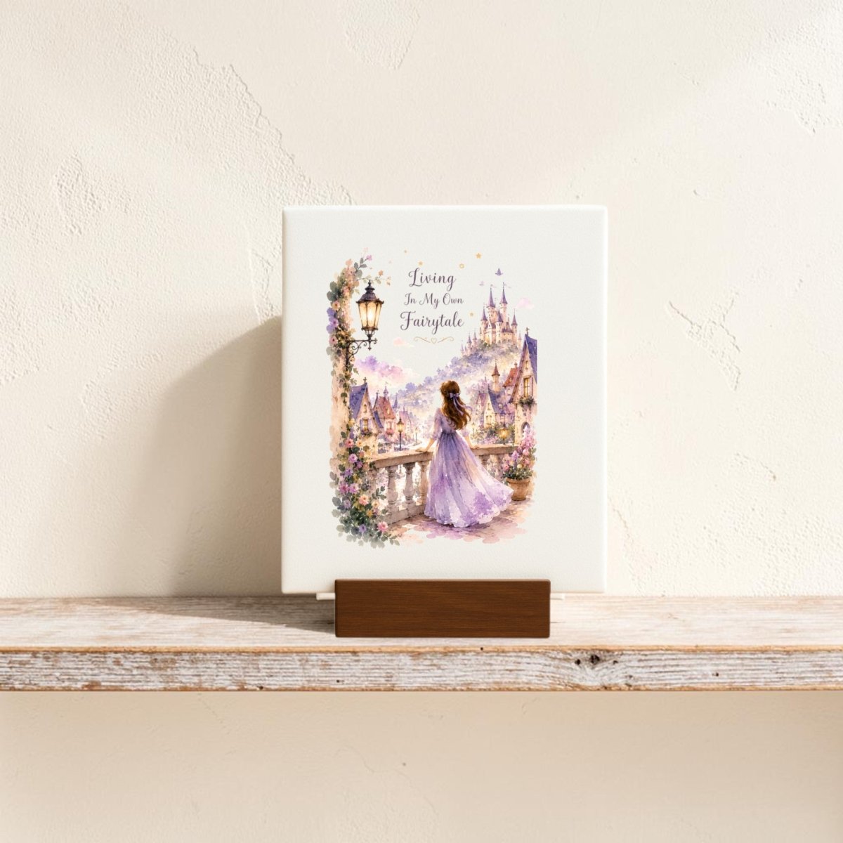The Living in My Own Fairytale Mini Canvas by Mirabilia Boutique features a woman in a purple gown gazing at a fairytale castle, with the words “Living in my own fairytale” above her. Detailed with flowers and soft pastel colors, this whimsical mini canvas is perfect as enchanting wall art or charming fairytale decor for your home.