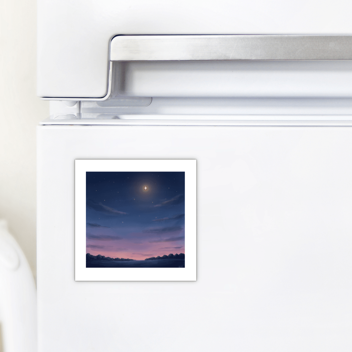 A small square print of a night sky with a bright star and clouds is attached near the top of a white refrigerator door by the handle, held securely in place with the Look Up Celestial Magnet from Mirabilia Boutique.