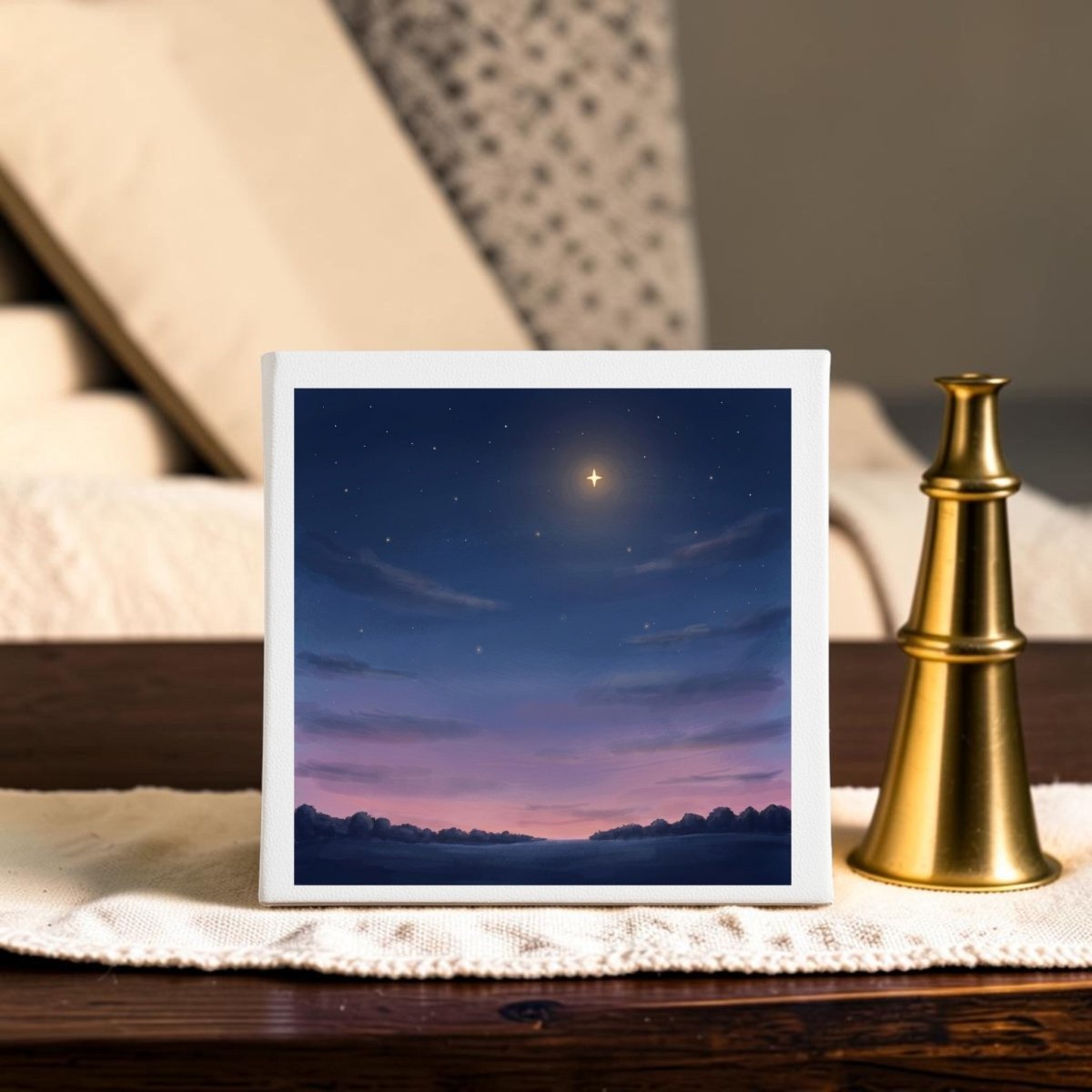 The Look Up Celestial Canvas Wall Art by Mirabilia Boutique, featuring a twilight sky with drifting clouds and a bright star, is framed and displayed on a wooden table beside a brass chess piece, with a beige couch in the background.