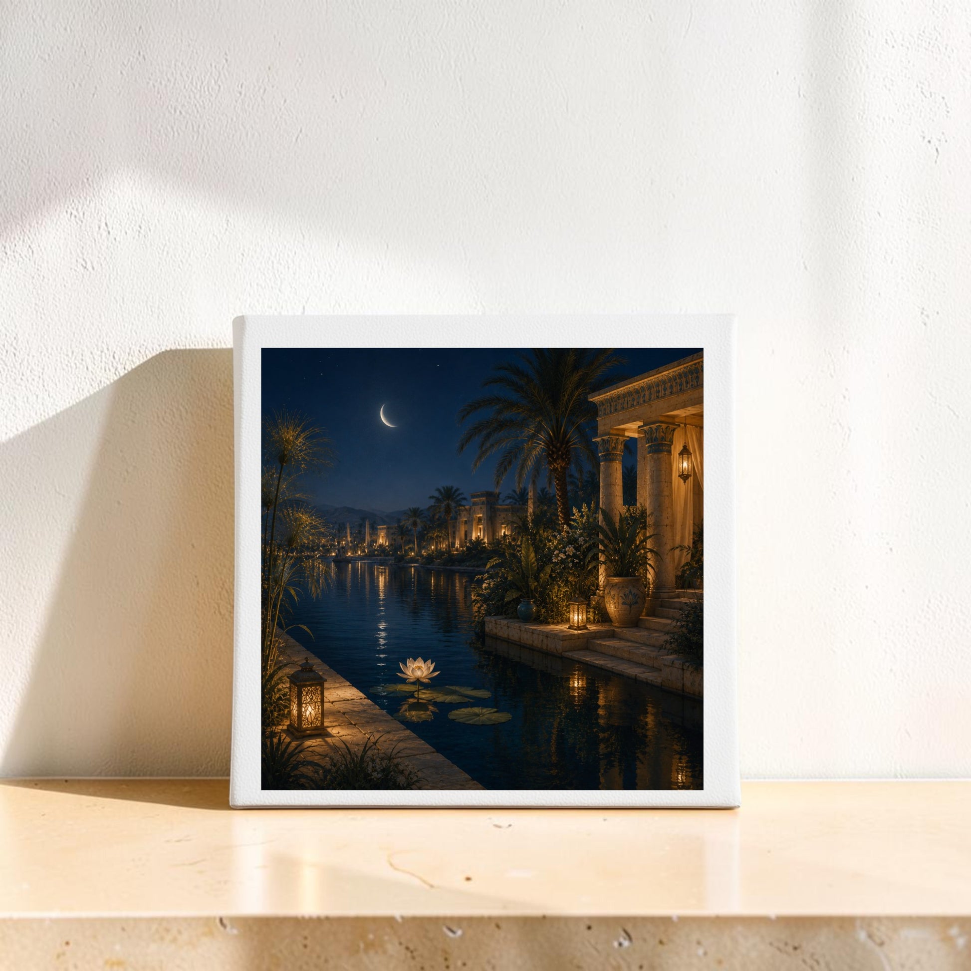 Lotus After Dark | Egyptian Canvas Wall Art by Mirabilia Boutique, featuring a moonlit canal with palm trees, ornate buildings, and glowing lanterns, is displayed on a light-colored shelf against a white wall.