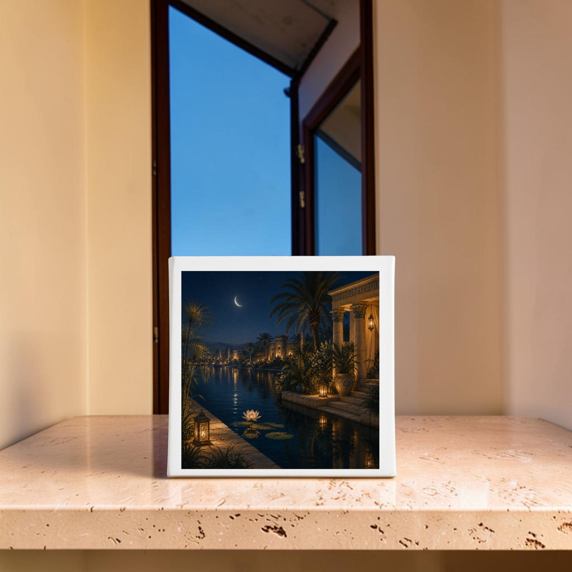 A framed print of “Lotus After Dark,” an Egyptian canvas wall art by Mirabilia Boutique, depicting a moonlit canal with palm trees, a crescent moon, and glowing lanterns, sits on a marble surface in front of an open window at dusk—evoking the tranquil beauty of the Nile.