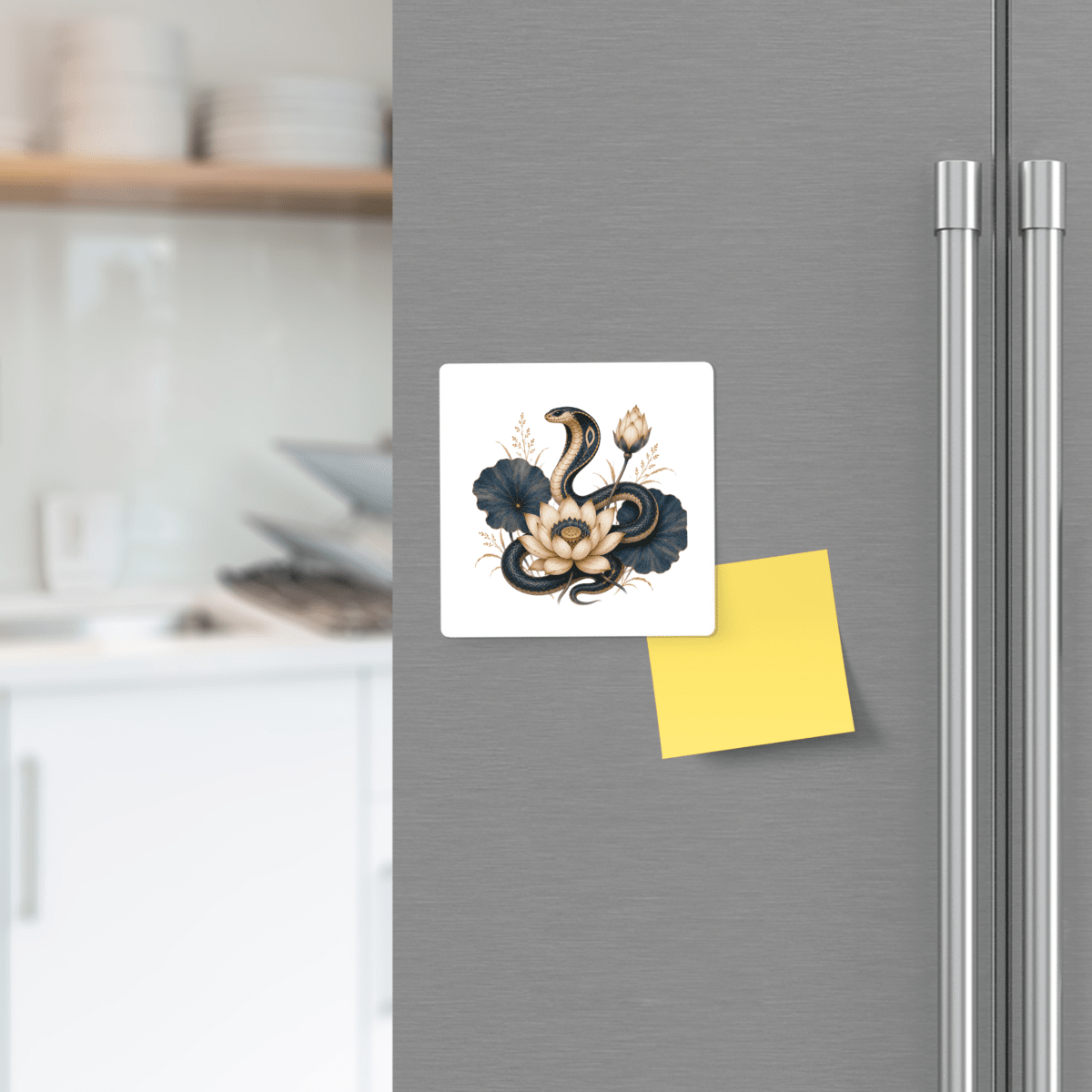 A refrigerator door displaying the Mirabilia Boutique “Lotus Guardian Cobra Magnet | Egyptian Lotus Art”—a square magnet featuring a snake and lotus flowers—sits beside a blank yellow sticky note, bringing a touch of Egyptian-inspired décor. In the background, dishes rest on the kitchen counter.