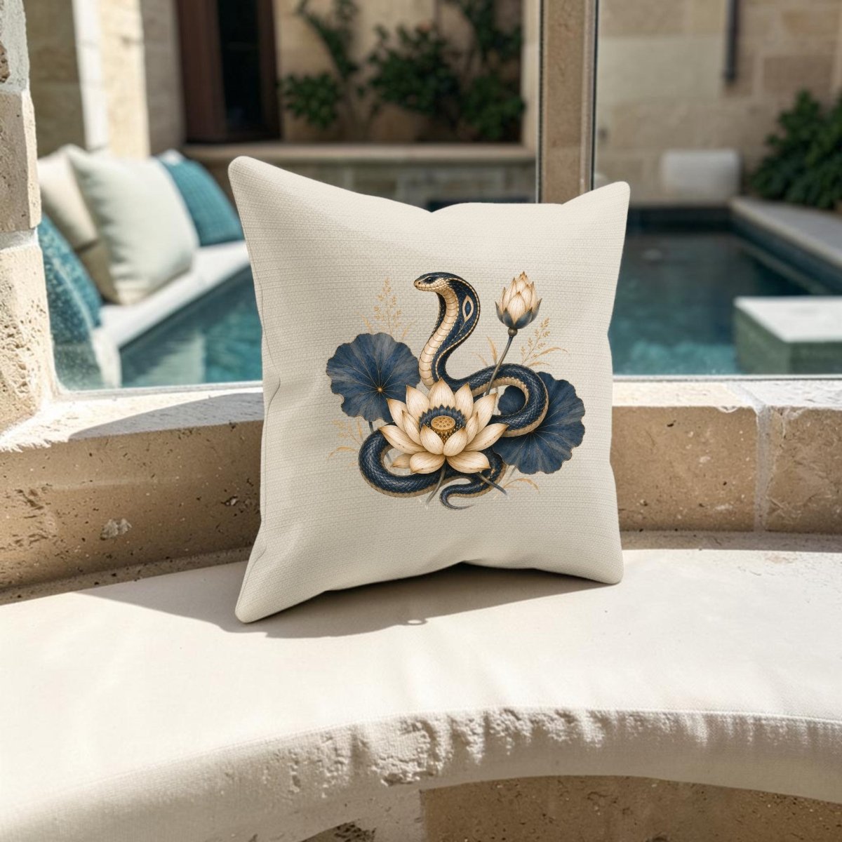 A cream-colored Lotus Guardian Cobra Pillow from Mirabilia Boutique, inspired by ancient Egyptian art, displays a dramatic black snake coiled around a lotus flower and rests on a curved outdoor bench near the pool.