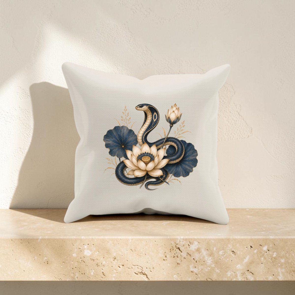 The Lotus Guardian Cobra Pillow | Ancient Egyptian Art by Mirabilia Boutique is a white throw pillow inspired by ancient Egyptian decor, adorned with an illustration of a coiled snake, white lotus flower, lotus bud, and dark blue leaves. It is displayed resting on a beige marble surface against a light textured wall.