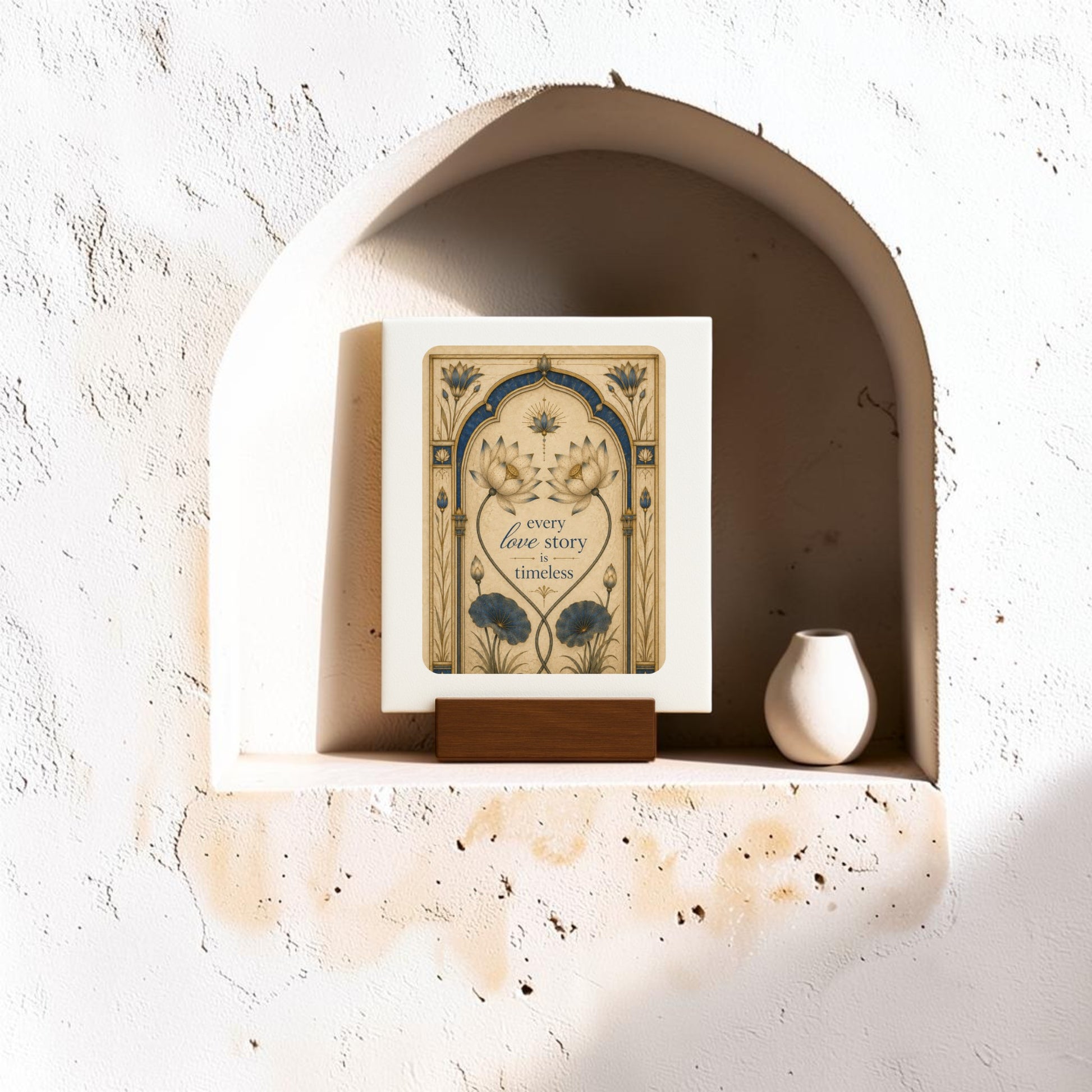 A decorative Lotus Mini Sign from Mirabilia Boutique, reading “Every Love Story Is Timeless,” stands on a wooden holder inside a wall niche next to a small white vase from the Mirabilia Lapis & Lotus Collection, all arranged on a textured, sunlit surface.