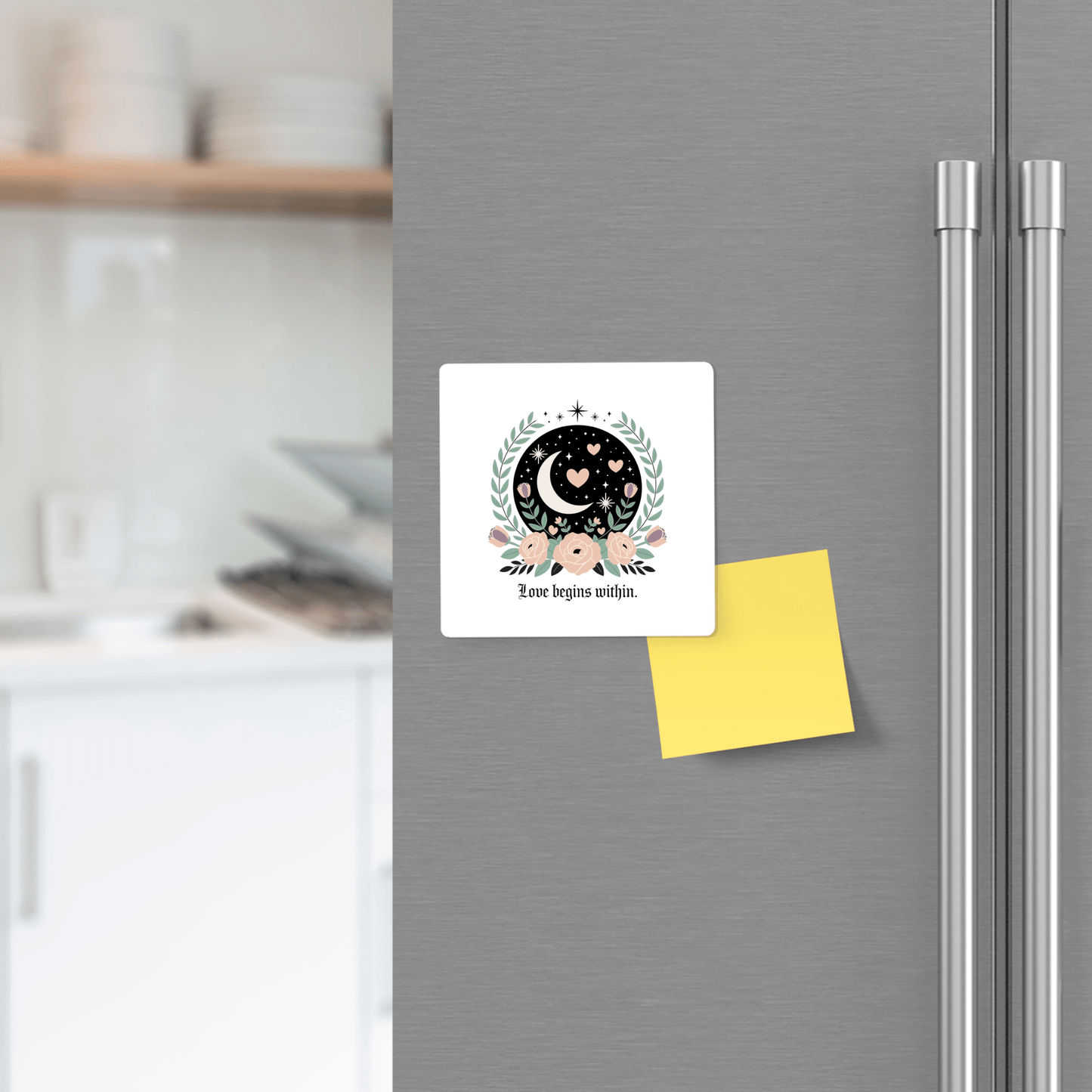The "Love Begins Within Magnet | Celestial Floral Self-Love Gift" by Mirabilia Boutique, featuring a whimsical moon and stars design, is displayed on a gray refrigerator door next to a blank yellow note in a modern kitchen.