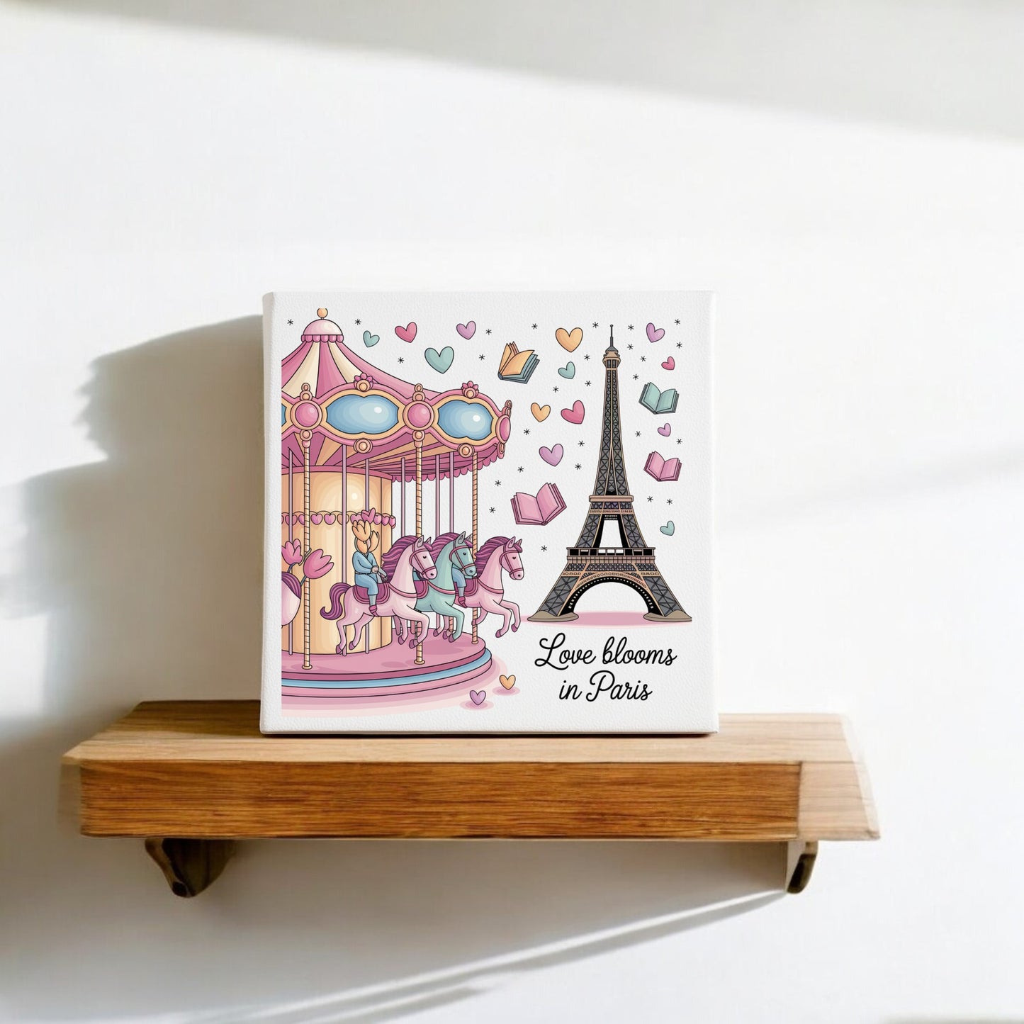 The Love Blooms in Paris Canvas by Mirabilia Boutique displays a romantic pastel scene with the Eiffel Tower and carousel. Sunlight casts gentle shadows as floating hearts and books add charm to this elegant wall art.