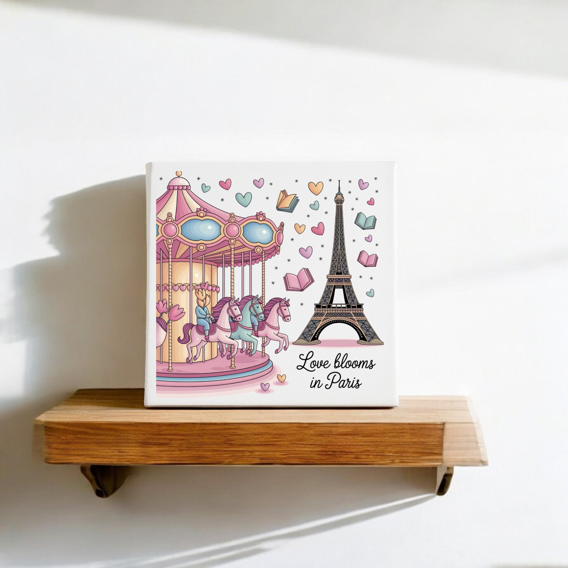 The Love Blooms in Paris Canvas by Mirabilia Boutique displays a romantic pastel scene with the Eiffel Tower and carousel. Sunlight casts gentle shadows as floating hearts and books add charm to this elegant wall art.
