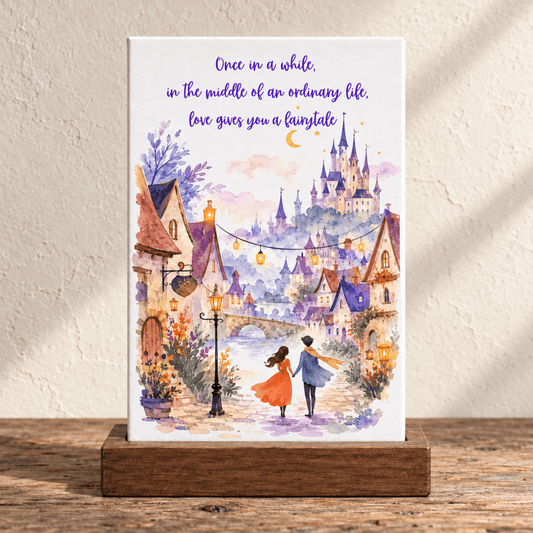A Love Gives You a Fairytale Mini Canvas Sign on a wooden stand features a romantic watercolor illustration of a couple walking toward a fairy-tale castle, inscribed with, “Once in a while, in the middle of an ordinary life, love gives you a fairytale.”